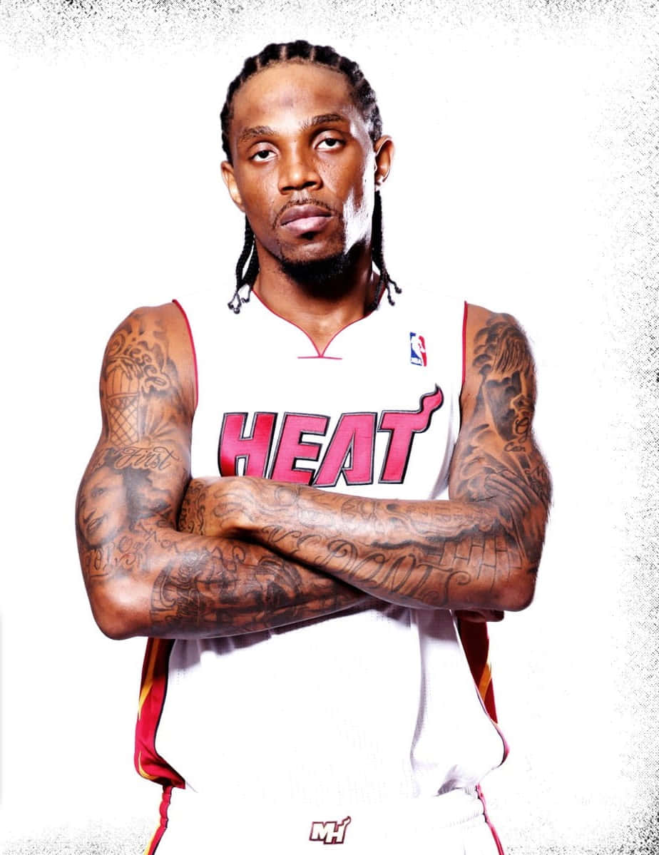 Udonis Haslem 桌布 壁紙 — 一名身穿邁阿密熱火球衣的籃球運動員，在帶有紋理的白色背景前自信地交叉雙臂站立。