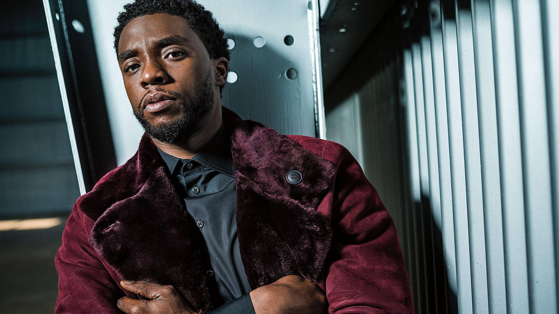 Chadwick 桌布 壁紙 — 一名身穿酒紅色天鵝絨外套的男子在戲劇性燈光下靠著金屬波紋牆。