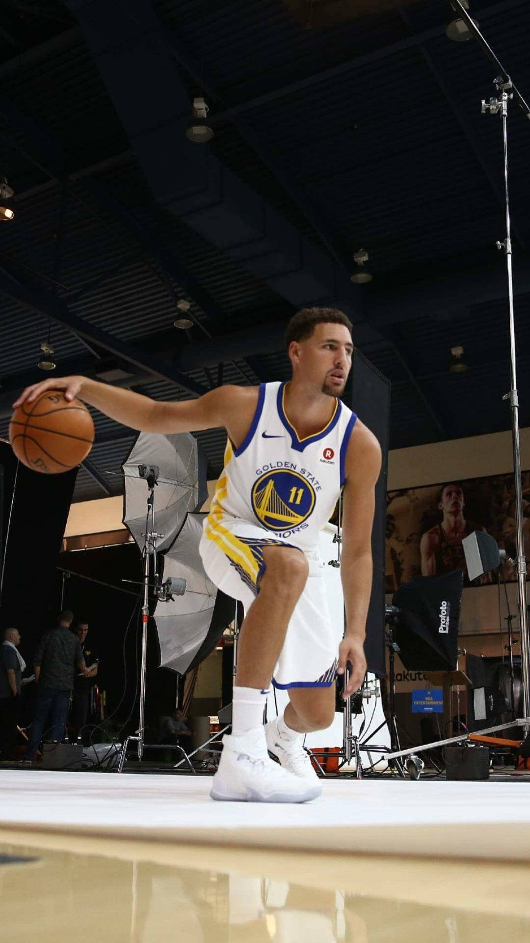 Thompson 桌布 壁紙 — 一名身穿金州勇士隊球衣的籃球運動員，在佈滿燈光設備的攝影棚地板上運球。