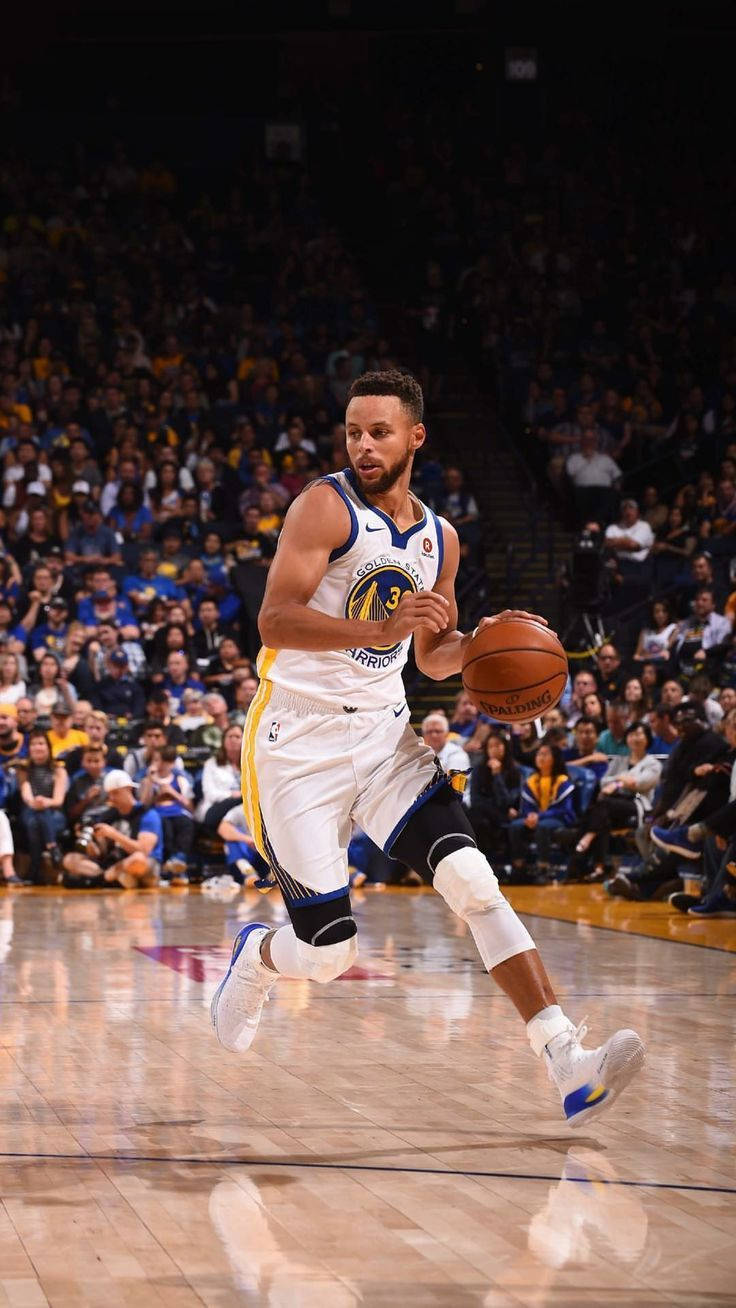 Curry 桌布 壁紙 — 一名身穿金州勇士隊球衣的籃球運動員在拋光球場上跨步運球，背景是座無虛席的體育館。