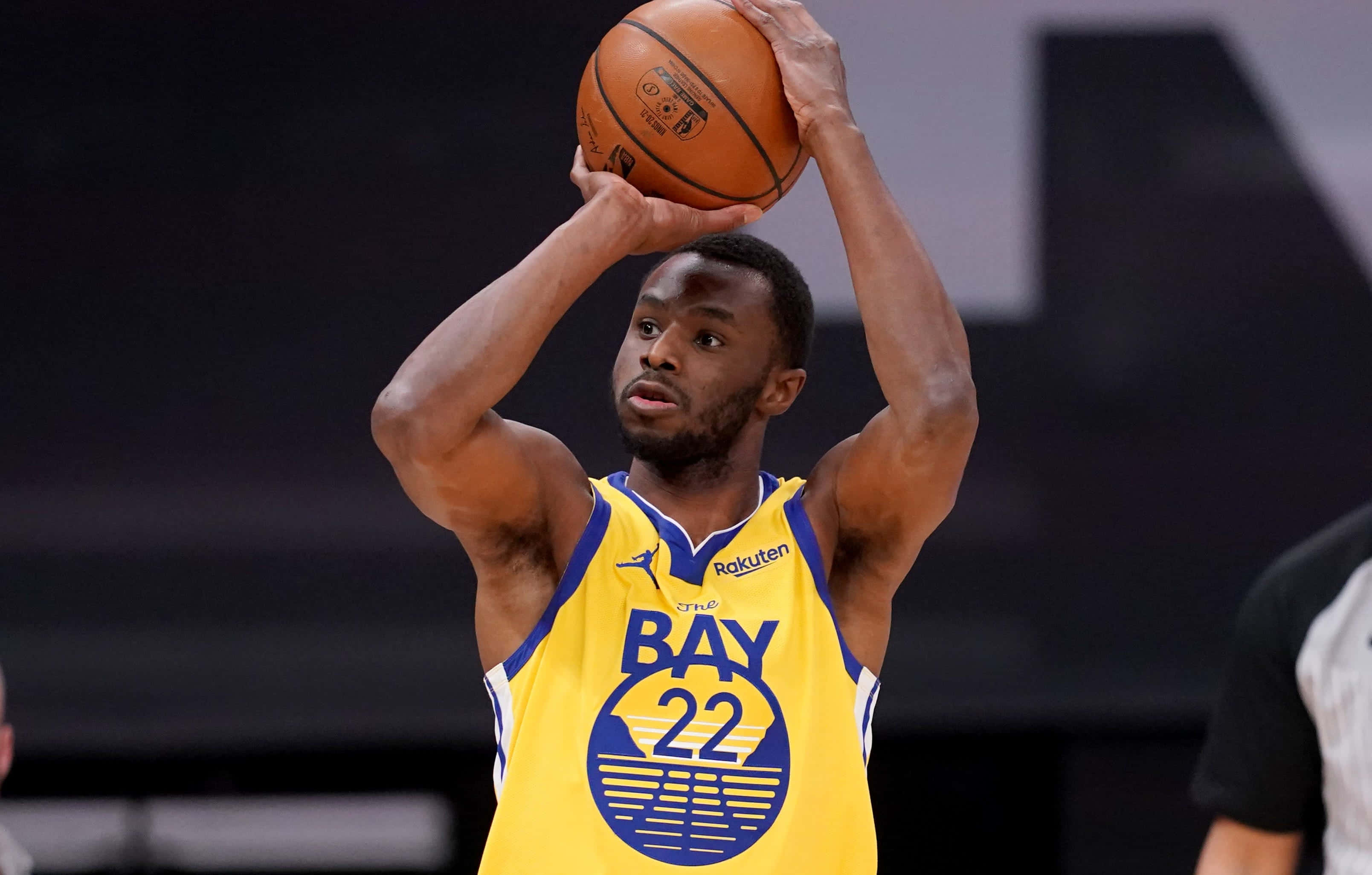 Andrew Wiggins 桌布 壁紙 — 一名身穿金色金州勇士隊球衣的籃球運動員在明亮的場館燈光下準備在比賽中投籃。