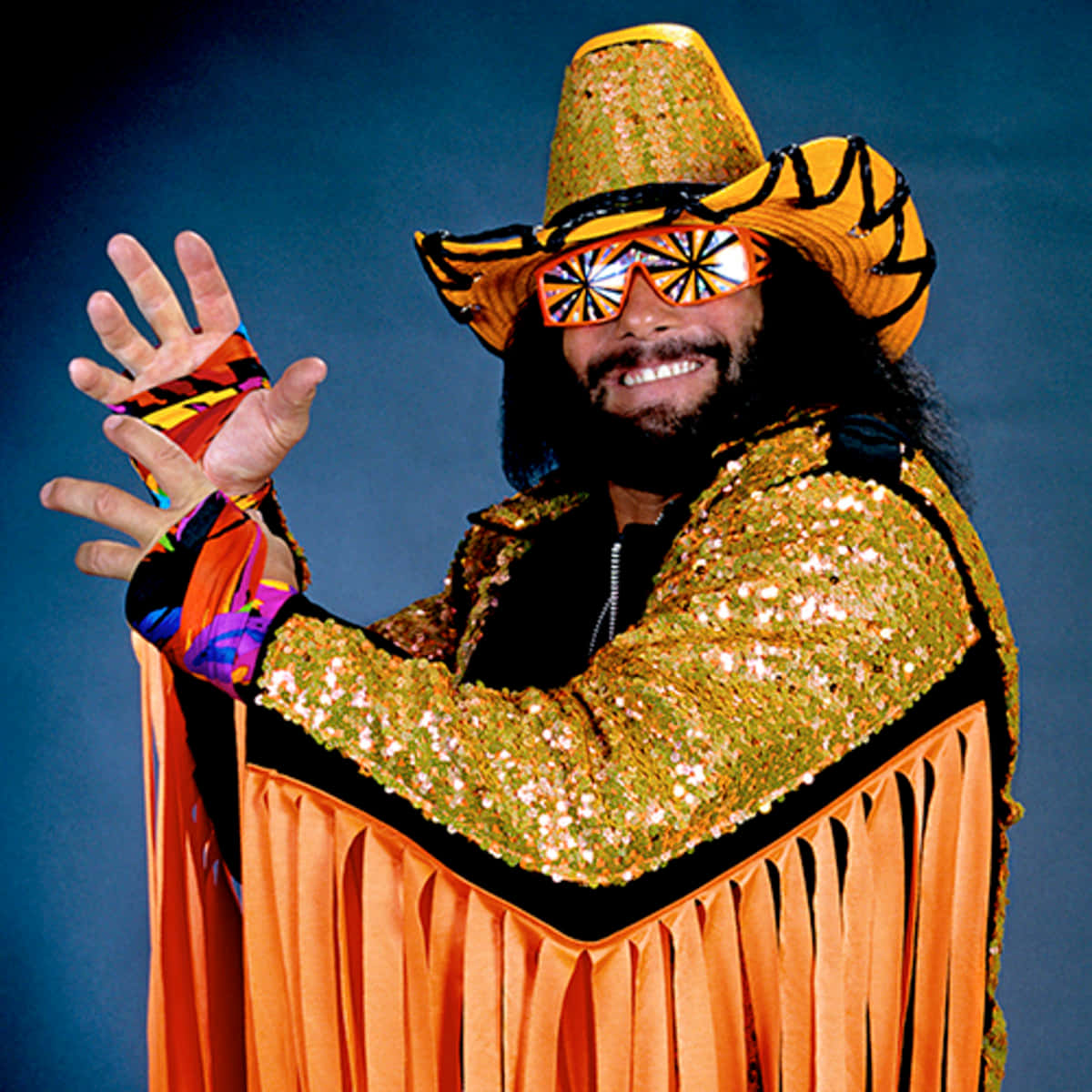 WWE 桌布 壁紙 — 一名身穿閃亮橙色亮片服裝和虎紋帽子的摔角手，在深藍色背景下愉快地揮手。
