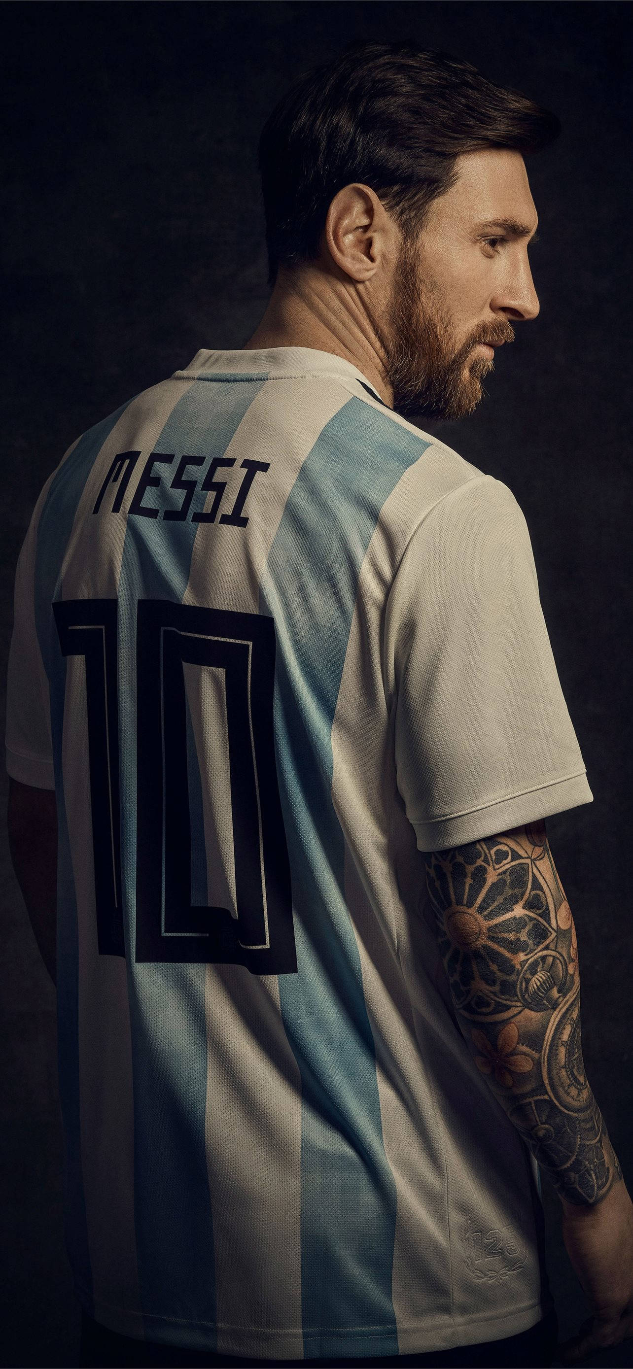 Messi 4K Ultra HD 桌布 壁紙 — 一名身穿阿根廷足球球衣、號碼10、有刺青手臂的男子在深色背景上轉頭。