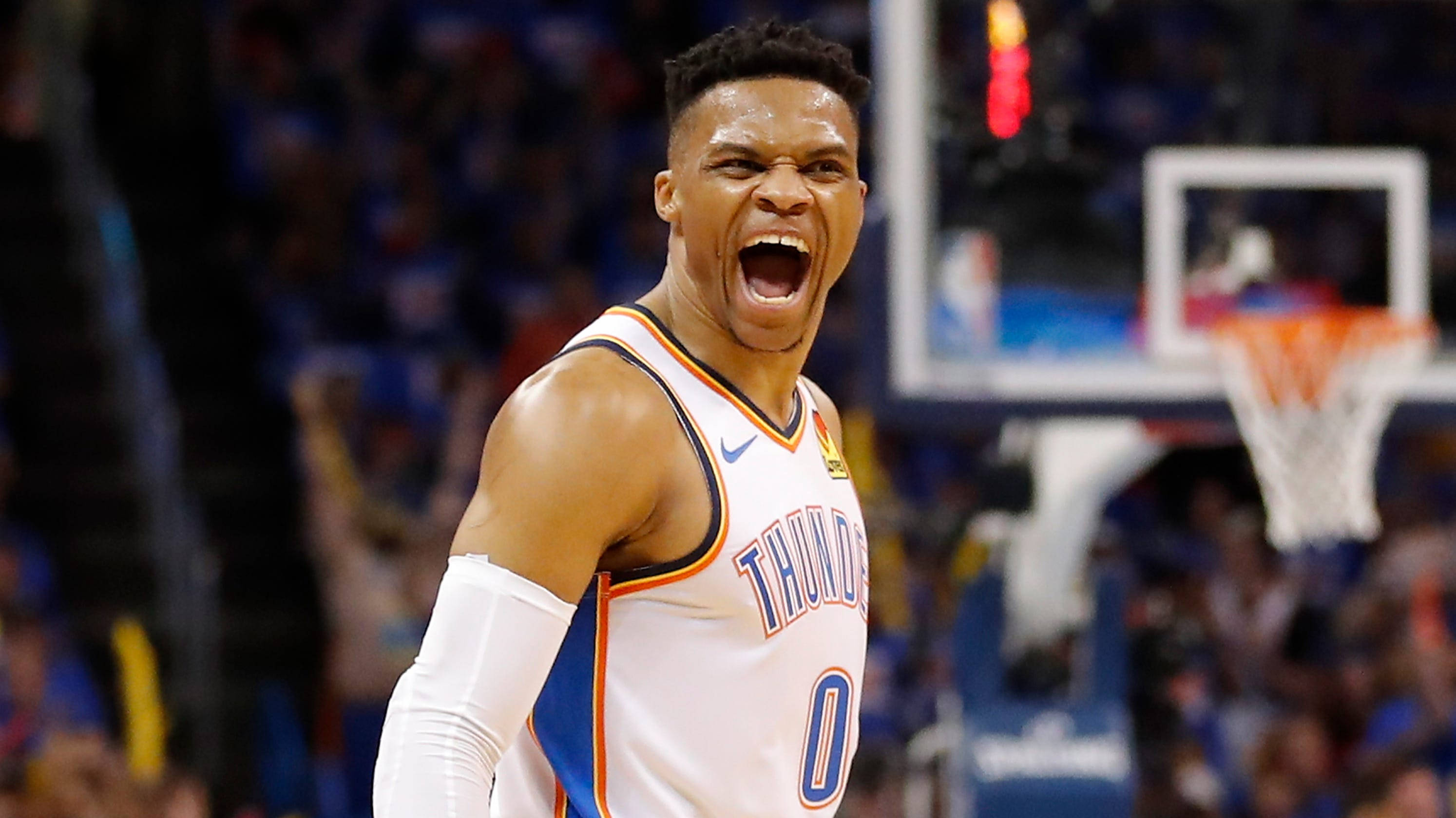 Westbrook 桌布 壁紙 — 一名身穿雷霆隊球衣的籃球運動員在燈光明亮的球場上，背景有籃框和人群，發出勝利的咆哮。