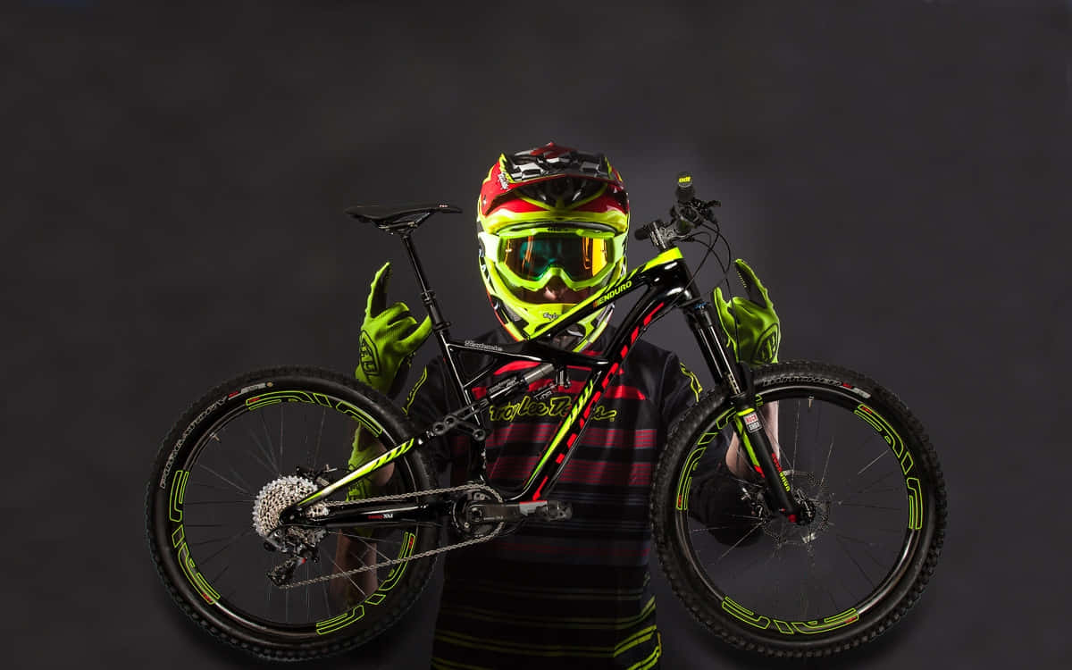Mountain Bike 桌布 壁紙 — 一名身穿霓虹裝備和頭盔的山地車手，在黑暗的攝影棚背景下，手持一輛帶有發光綠色點綴的黑色自行車。