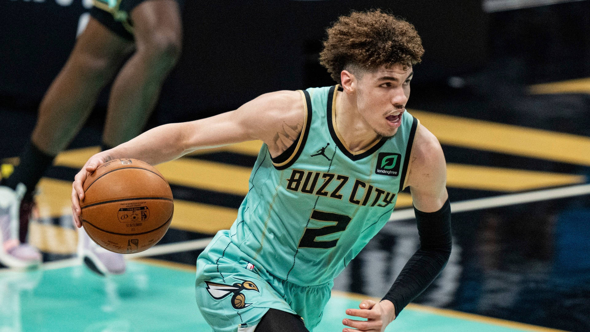 ball 桌布 壁紙 — 一名身穿青綠色「Buzz City」球衣的籃球運動員在明亮的場館燈光下於比賽中激烈運球。