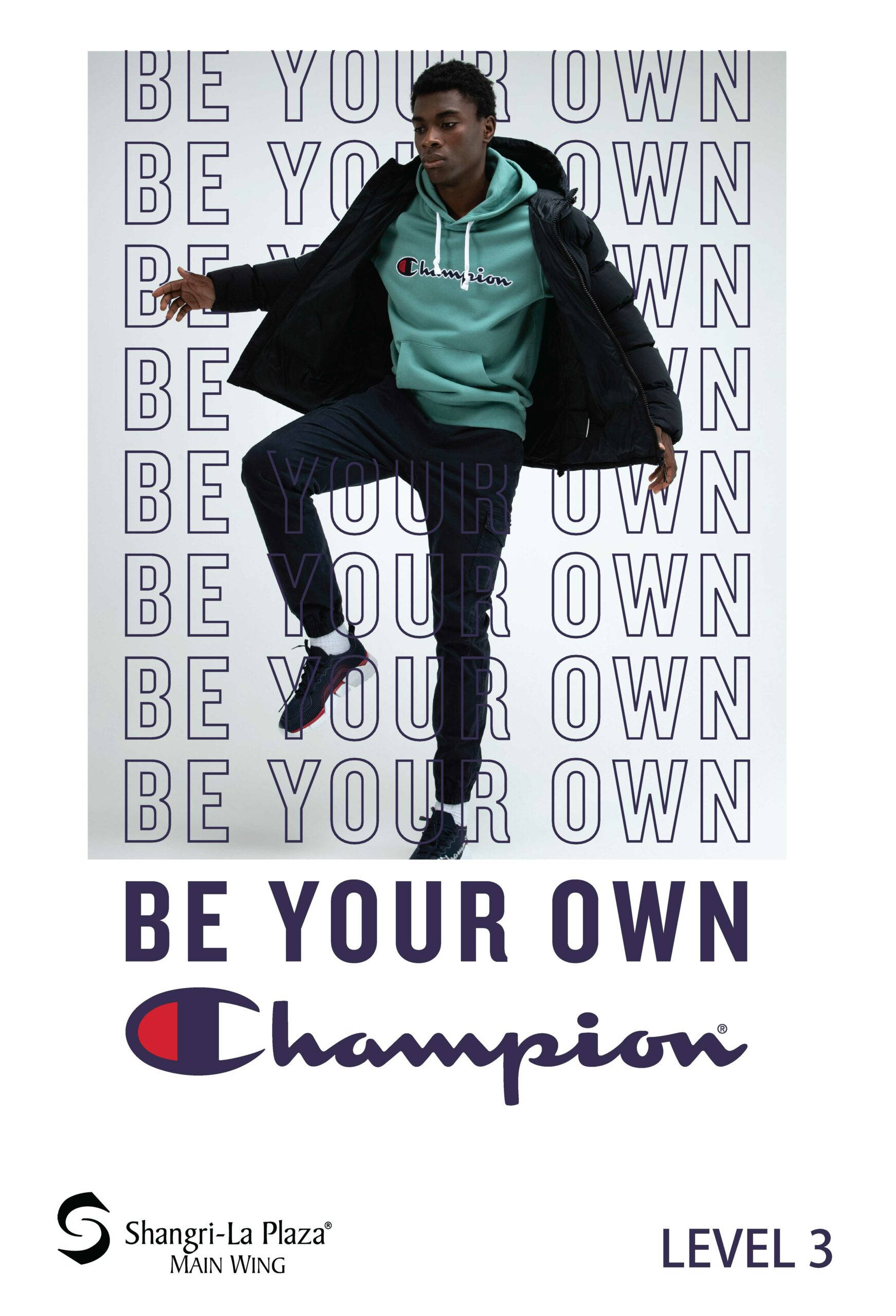 Champion 桌布 壁紙 — 一名身穿青綠色Champion連帽衫和黑色外套的年輕男子，在重複的「BE YOUR OWN」文字牆和下方品牌標誌前擺出動態姿勢。