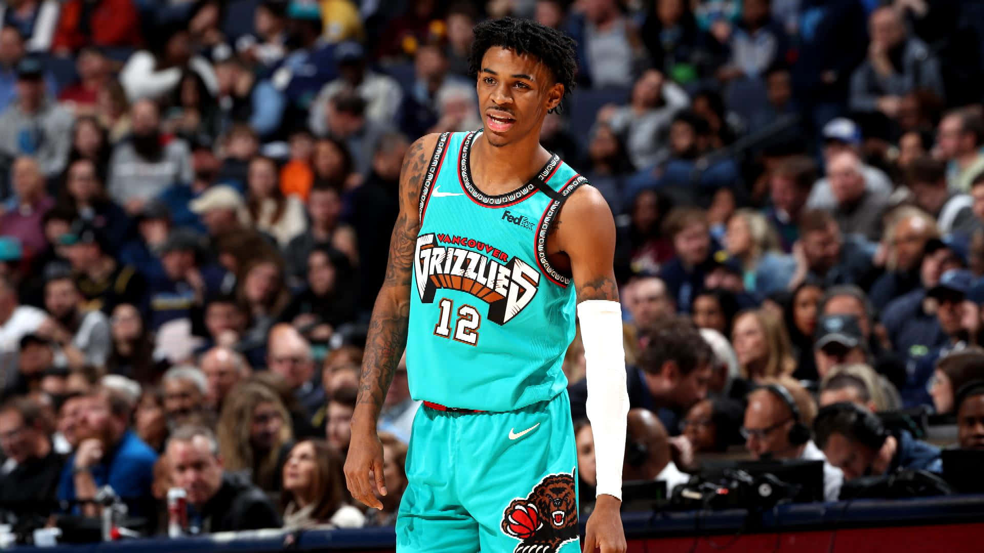 Ja Morant 動圖 桌布 壁紙 — 一名身穿青綠色溫哥華灰熊隊球衣的籃球運動員站在球場上，背景有觀眾。