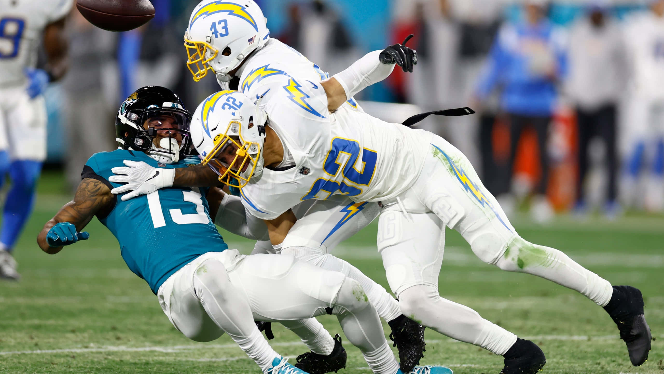 Sports 4K 桌布 壁紙 — 一名身穿青綠色球衣的足球員飛身撲向球，兩名身穿白色球衣的防守球員在充滿活力的綠色球場上攔截他。
