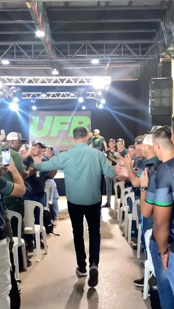 MMA 桌布 壁紙 — 一名身穿青綠色襯衫的男子在明亮的舞台燈光下，走過一條兩旁都是歡呼的粉絲、手持手機的通道。