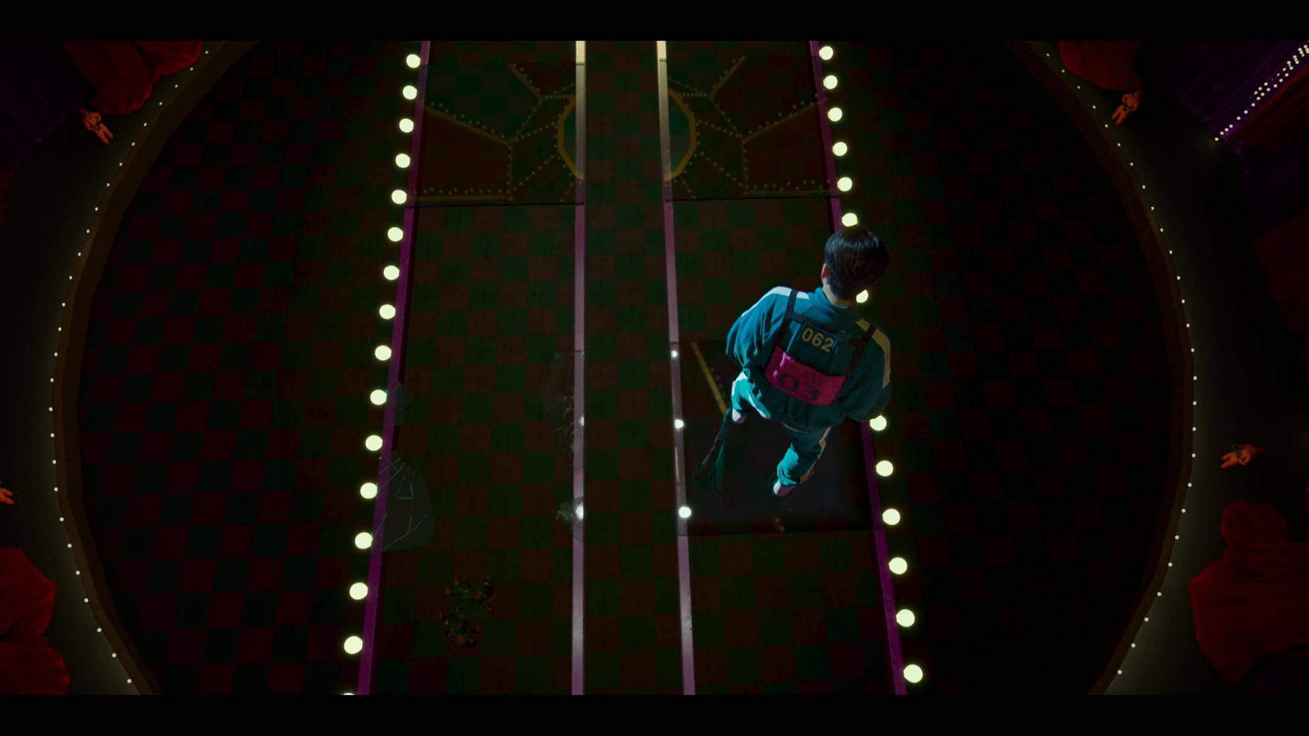 game 桌布 壁紙 — 一名身穿青綠色運動服的參賽者在燈光昏暗的競技場中，沿著燈光明亮的格子跑道奔跑。