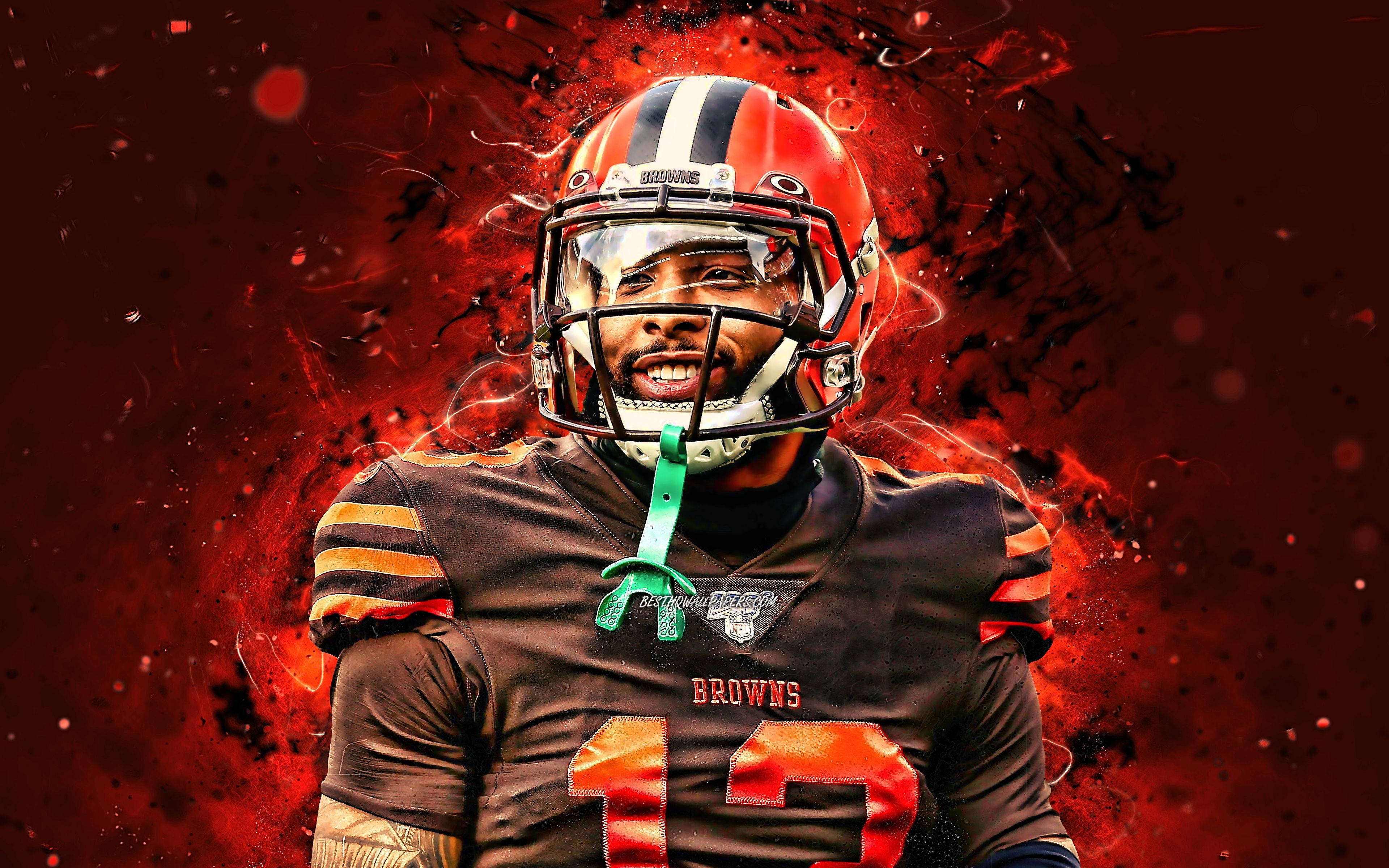 Odell 桌布 壁紙 — 一名身穿頭盔和球衣的克里夫蘭布朗隊美式足球員，站在熾熱的紅色爆炸背景前，周圍有發光的粒子。