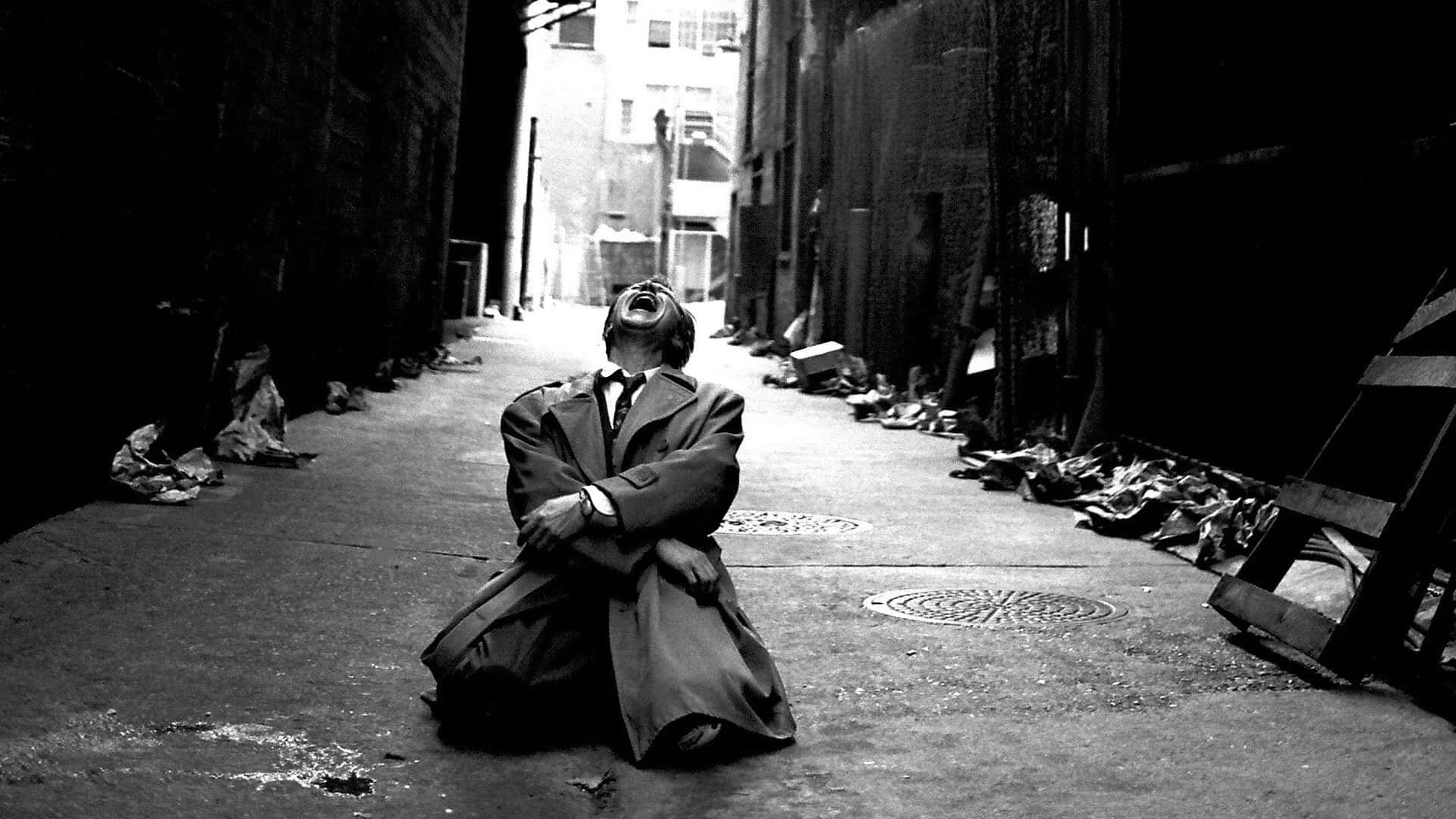 Sad Face 桌布 壁紙 — 一名身穿風衣的男子在骯髒的城市後巷跪下，頭部向後傾，呈現鮮明的黑白效果。
