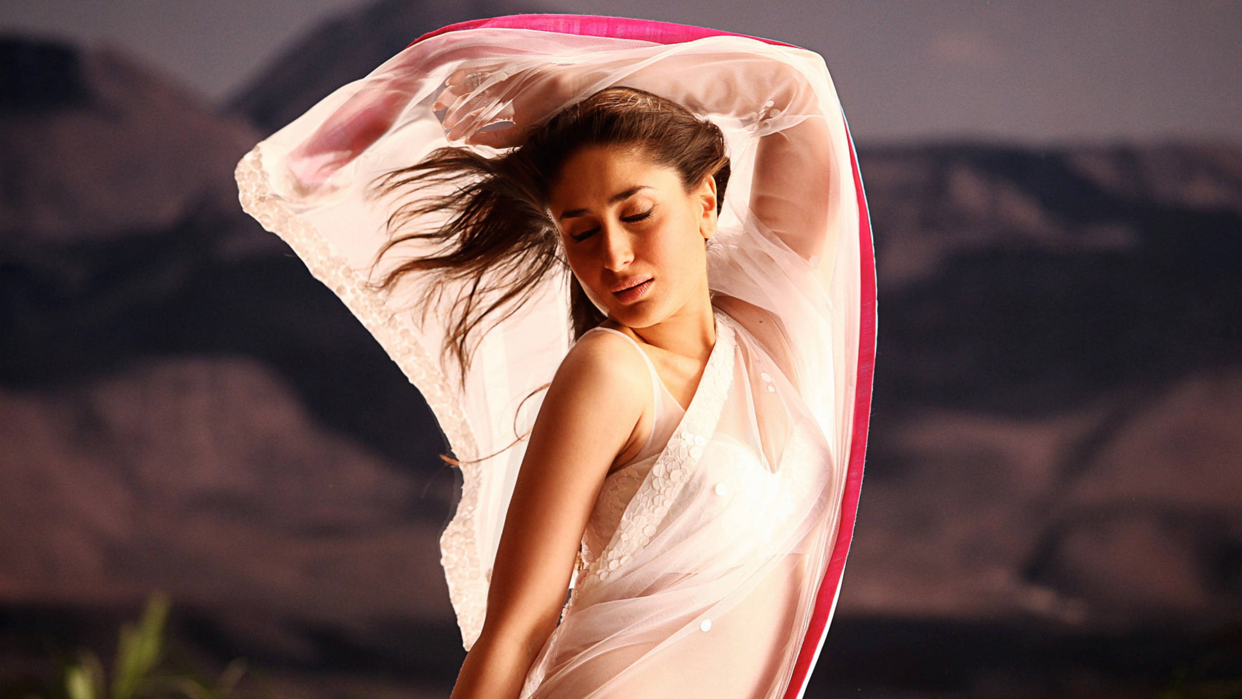 Kareena 桌布 壁紙 — 一名身穿飄逸白色和粉紅色服飾的女子，在暮色蒼茫的山巒背景下優雅地跳舞。