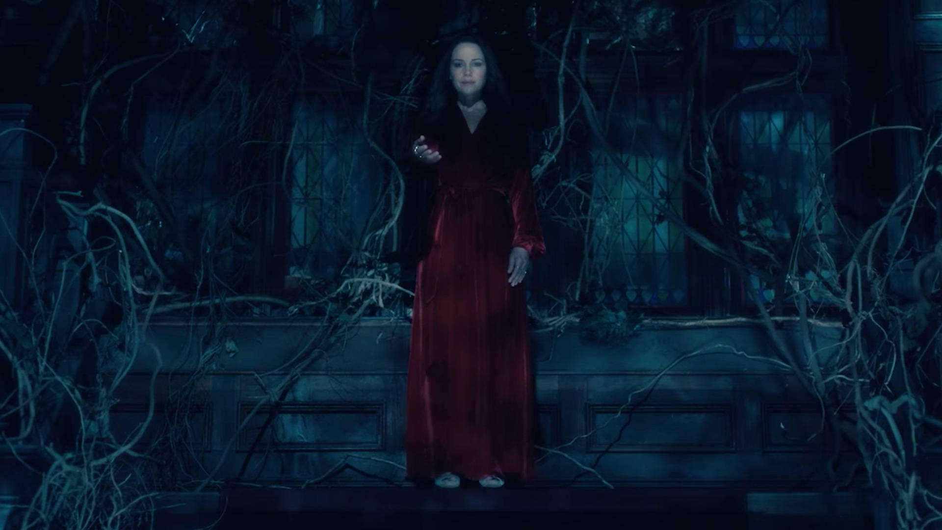 Haunting 桌布 壁紙 — 一名身穿飄逸紅裙的女子，在詭異的藍色月光下，莊嚴地站在藤蔓纏繞的門廊上。