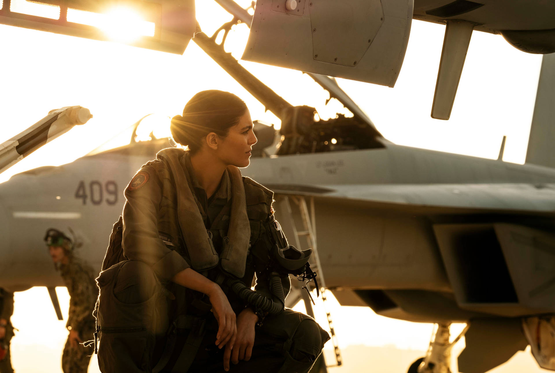 女飛行員穿著飛行服坐在戰鬥機旁，夕陽映照。 — 捍衛戰士：獨行俠 壁紙