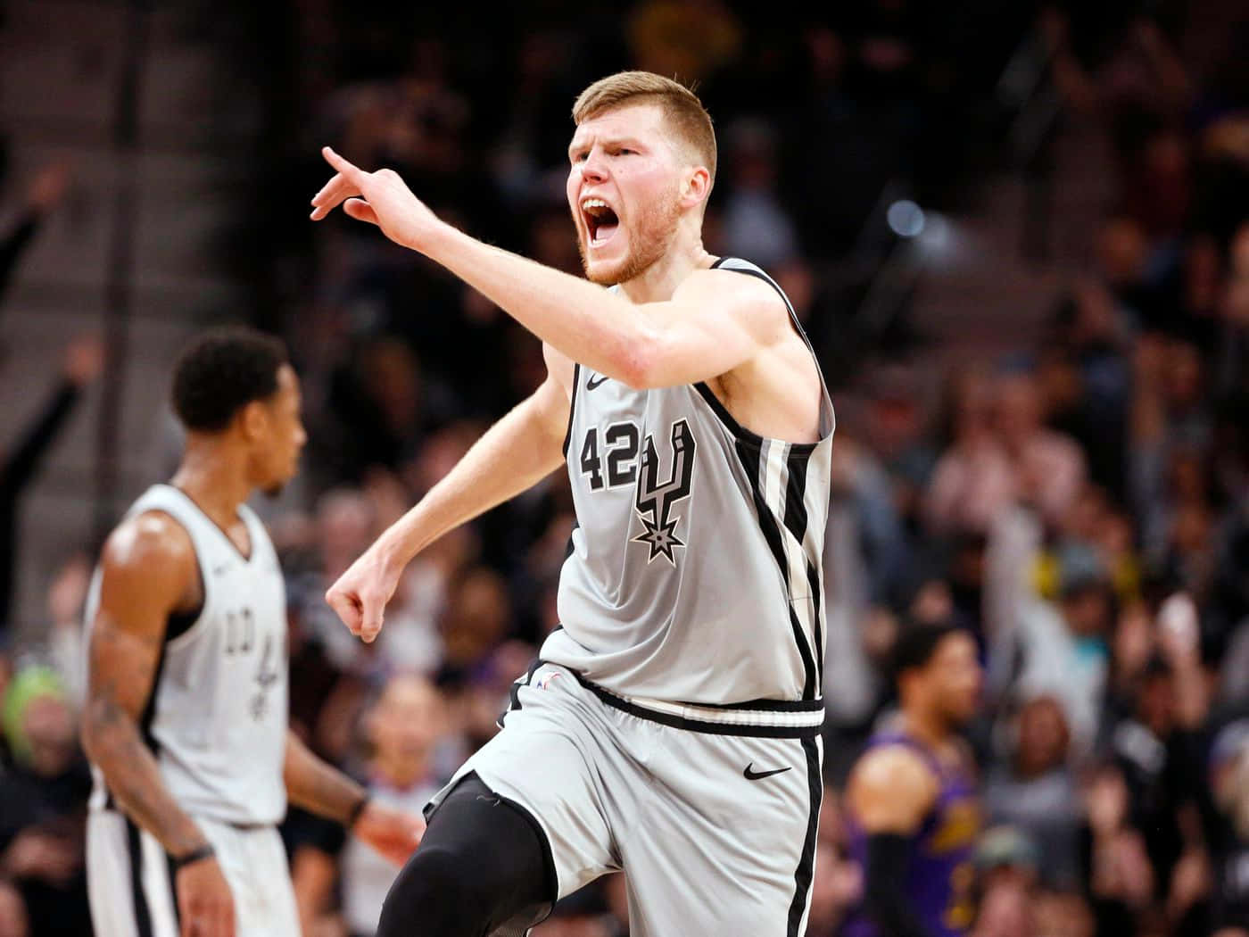 NBA標誌 桌布 壁紙 — 一名身穿馬刺球衣的籃球運動員在比賽中尖叫並勝利地指向遠方，身後是模糊的人群。