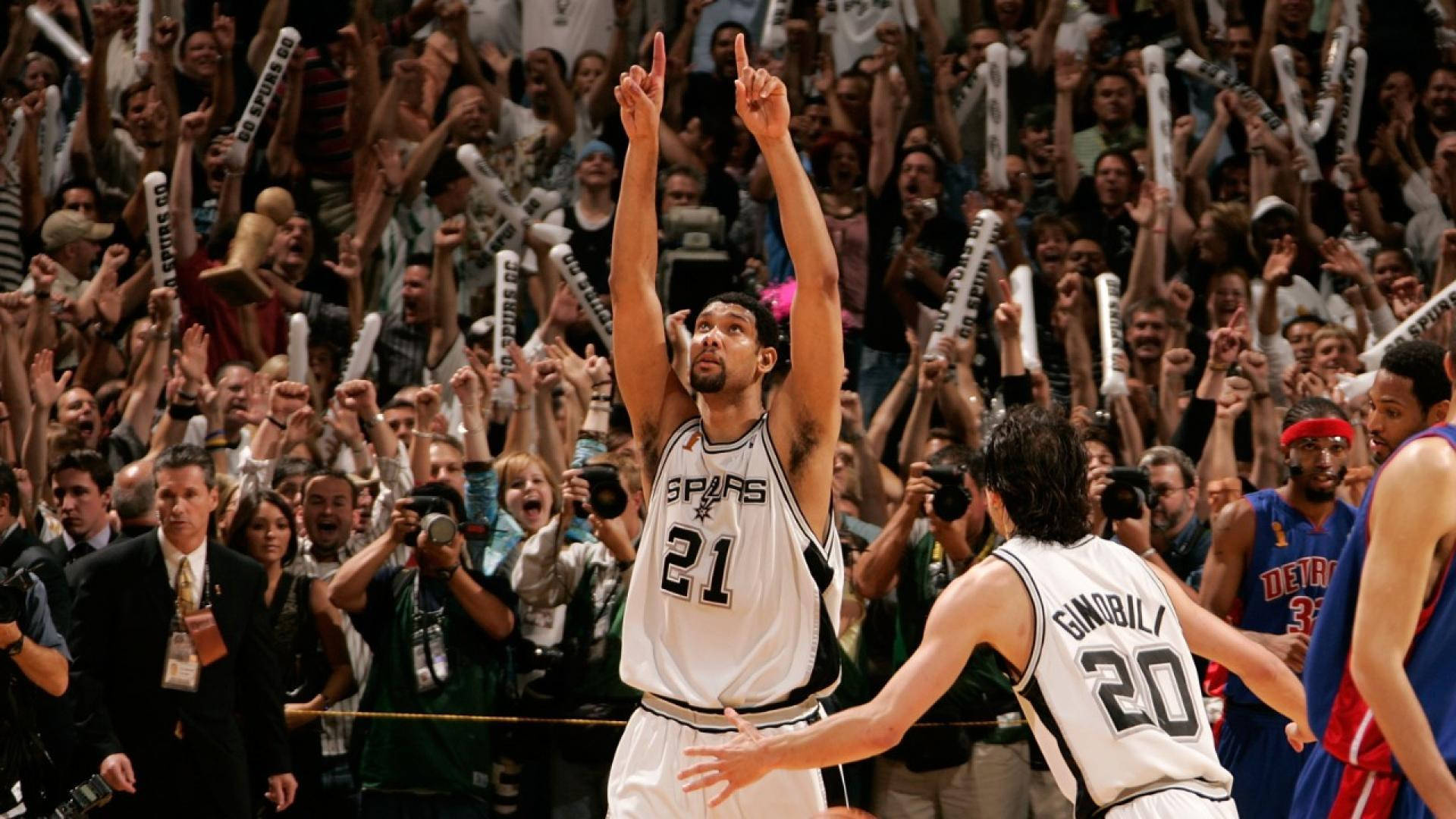 NBA總決賽 桌布 壁紙 — 一名身穿馬刺隊球衣的籃球運動員勝利地舉起雙食指，看台上的球迷揮舞著泡沫手指瘋狂歡呼。