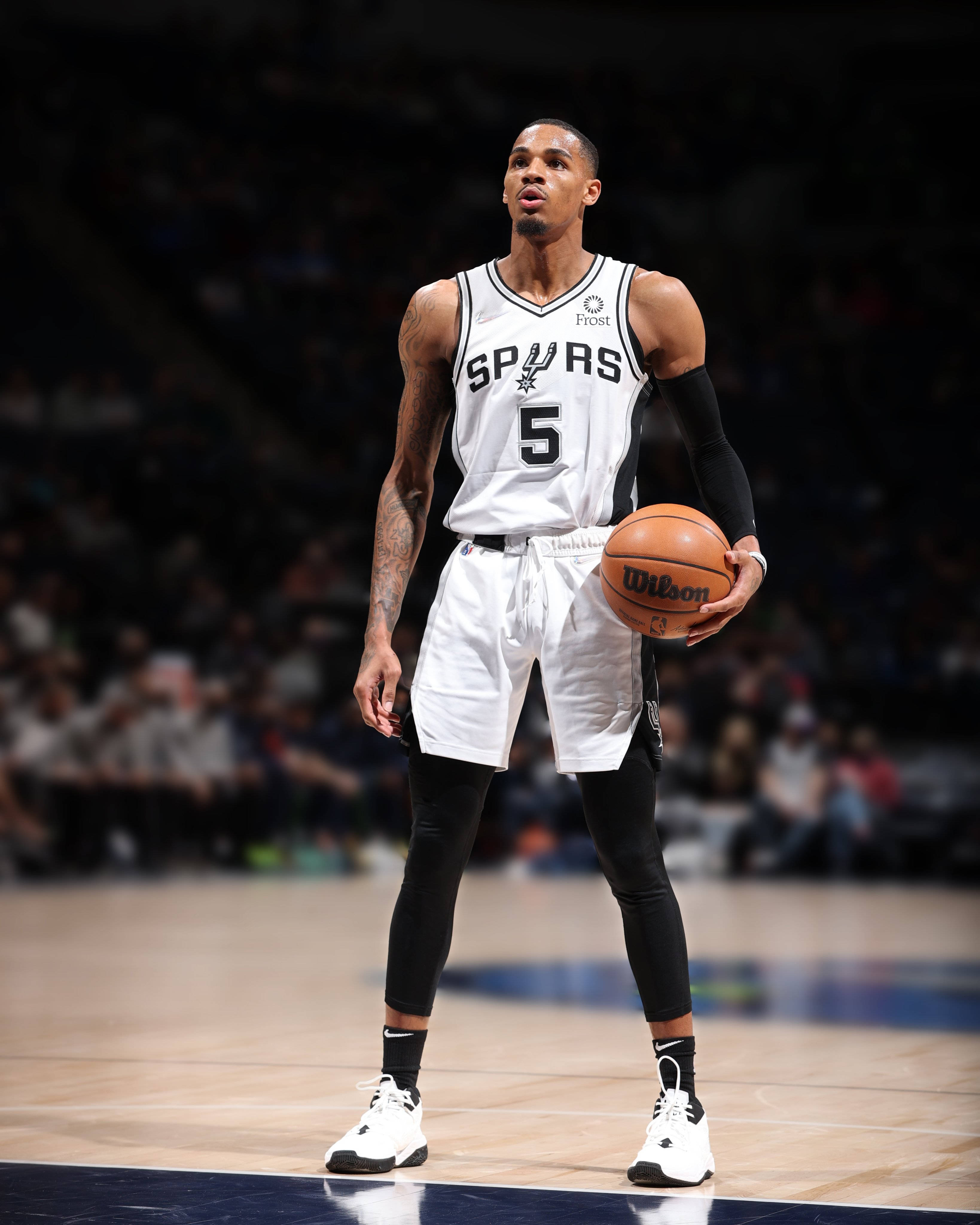 Dejounte Murray 桌布 壁紙 — 一名身穿馬刺隊球衣的籃球運動員在場館燈光下、模糊觀眾背景中，於球場上持球。