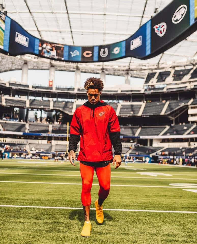 Byron Murphy 桌布 壁紙 — 一名身穿鮮紅色和黃色裝備的美式足球運動員在明亮的日光下自信地走過空無一人的球場。