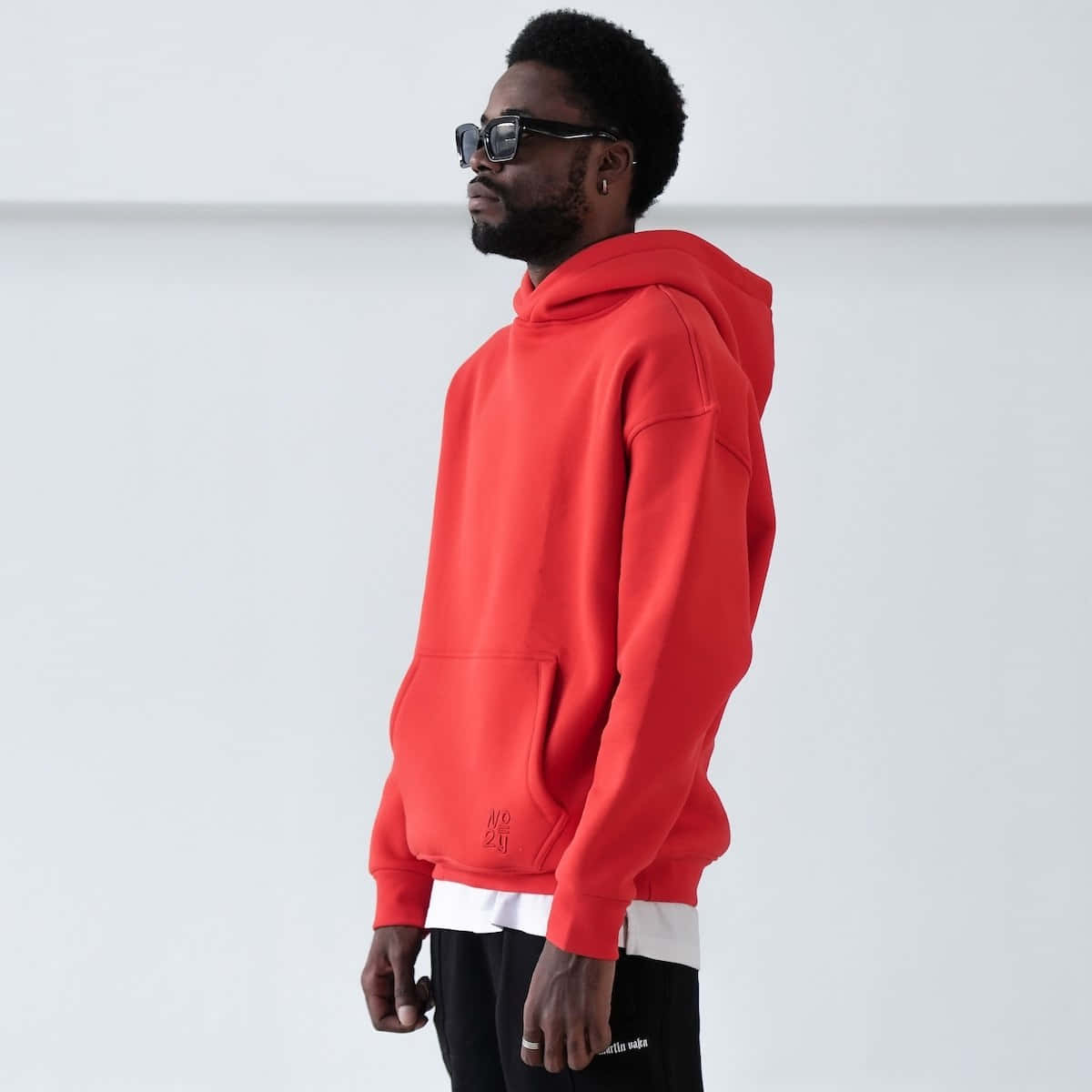 Red Hoodie 桌布 壁紙 — 一名身穿鮮紅色連帽上衣和黑色太陽眼鏡的男子，在極簡白色背景前側面站立。