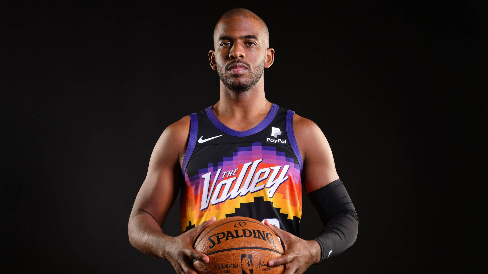 sport 桌布 壁紙 — 一名身穿鮮豔Suns球衣的籃球運動員，在純黑背景下手持Spalding籃球。
