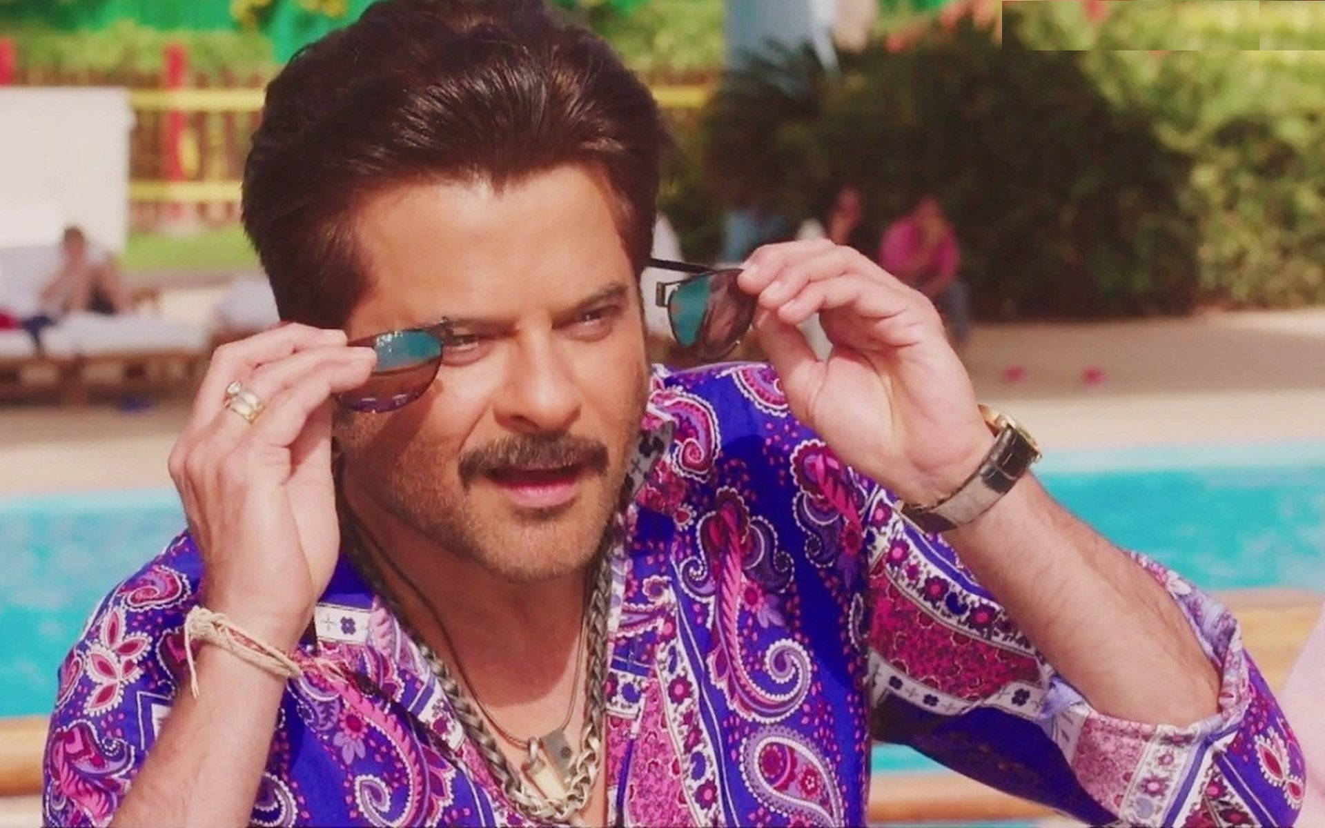 anil kapoor 桌布 壁紙 — 一名身穿鮮豔佩斯利花紋襯衫的男子，在明媚陽光下於游泳池旁脫下太陽眼鏡。