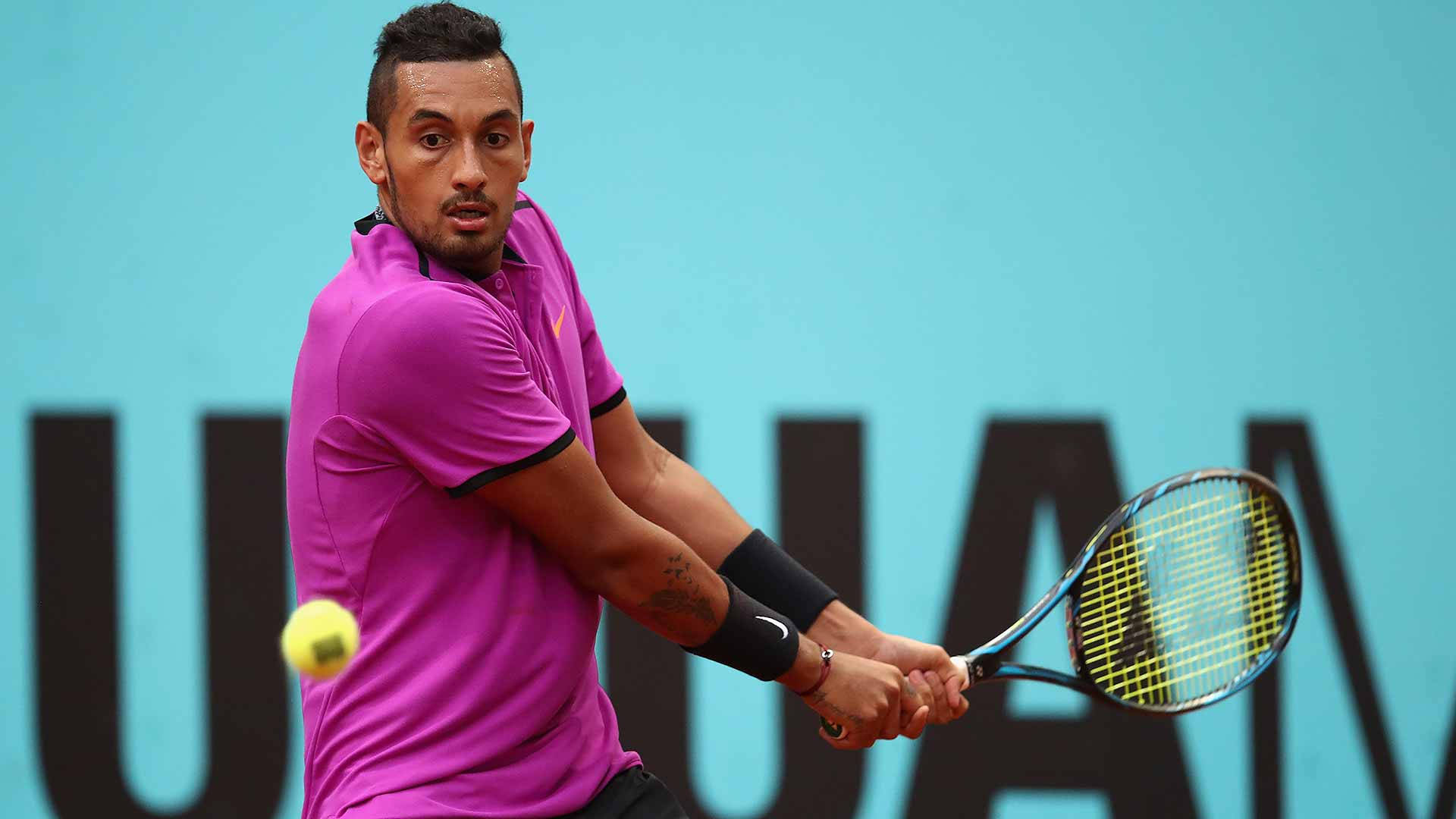 Kyrgios 桌布 壁紙 — 一名身穿鮮豔粉紅色襯衫的男性網球選手，在帶有粗體黑色字樣的青綠色牆壁前，揮拍擊打一個黃色網球。