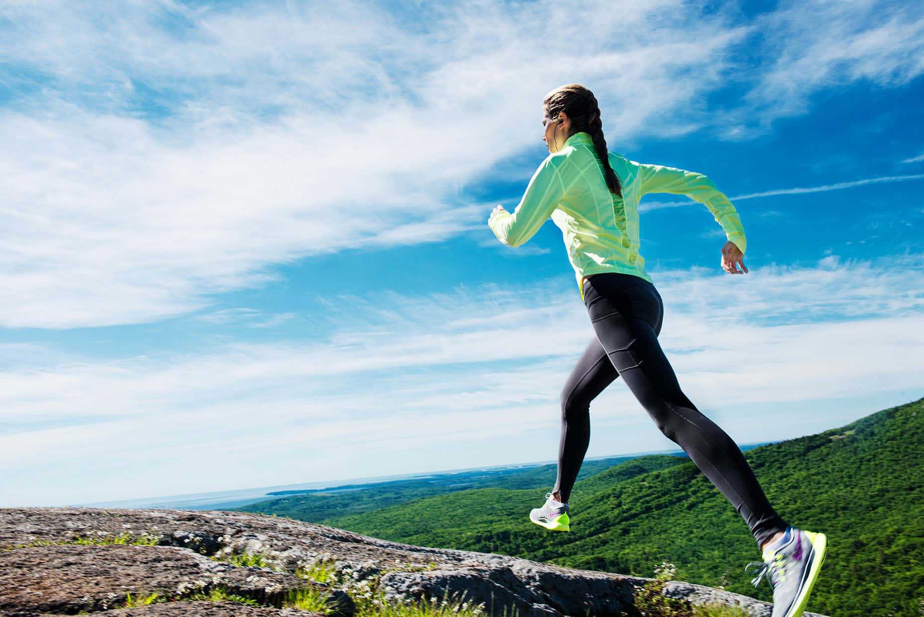 Fitness 桌布 壁紙 — 一名身穿鮮豔螢光跑步裝備的女性，在廣闊藍天白雲下，飛奔過岩石山頂。