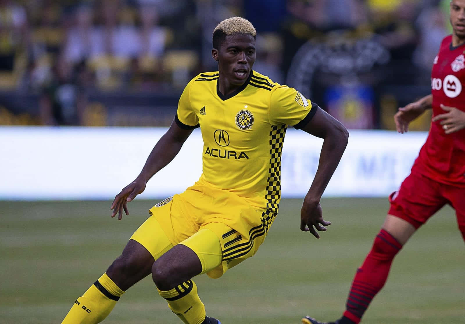 Columbus Crew 桌布 壁紙 — 一名身穿鮮黃色球衣的足球運動員在日間比賽中，專注地衝過綠色球場。