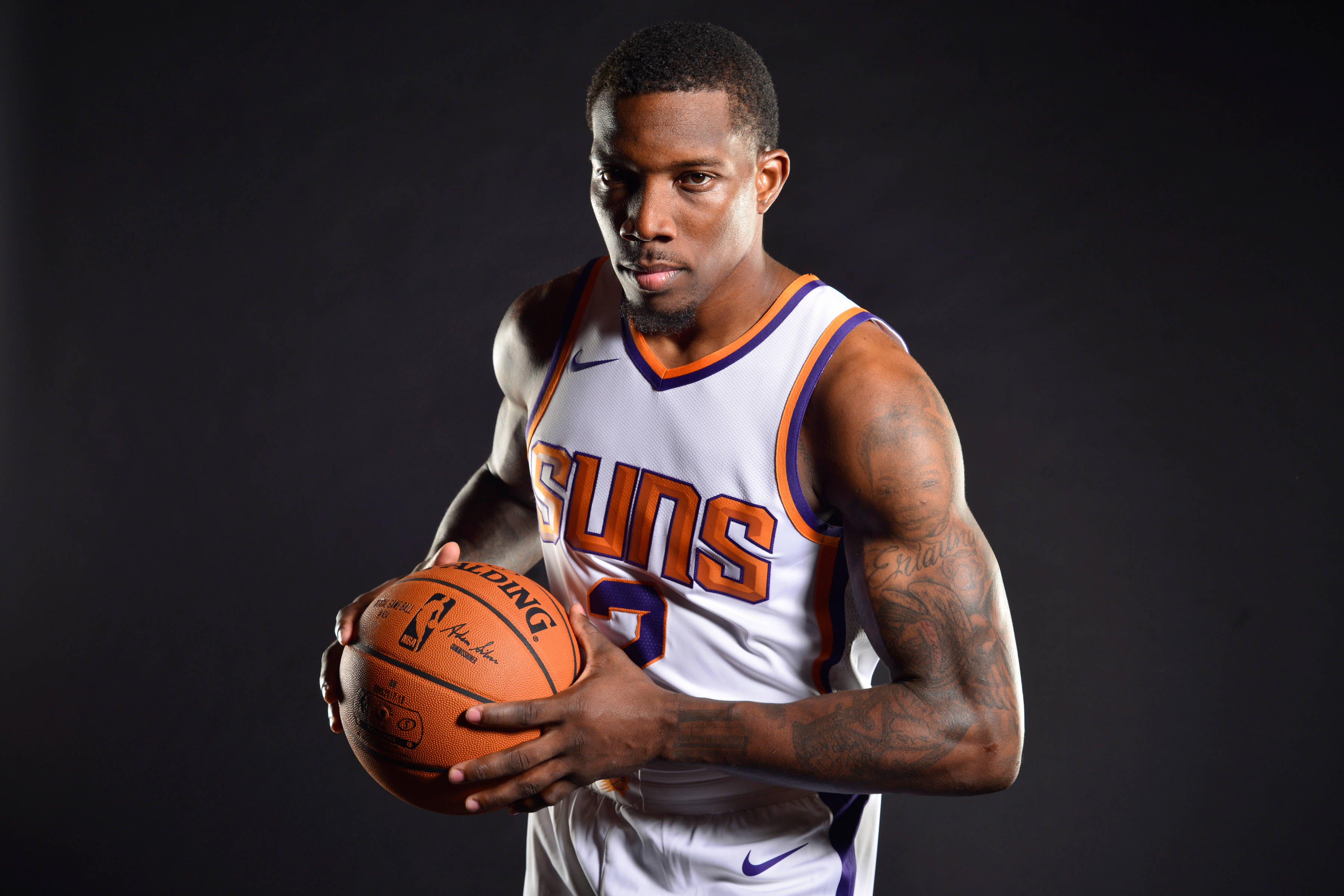 eric bledsoe 桌布 壁紙 — 一名身穿鳳凰城太陽隊球衣的籃球運動員，在深色工作室背景下專注地拿著球。