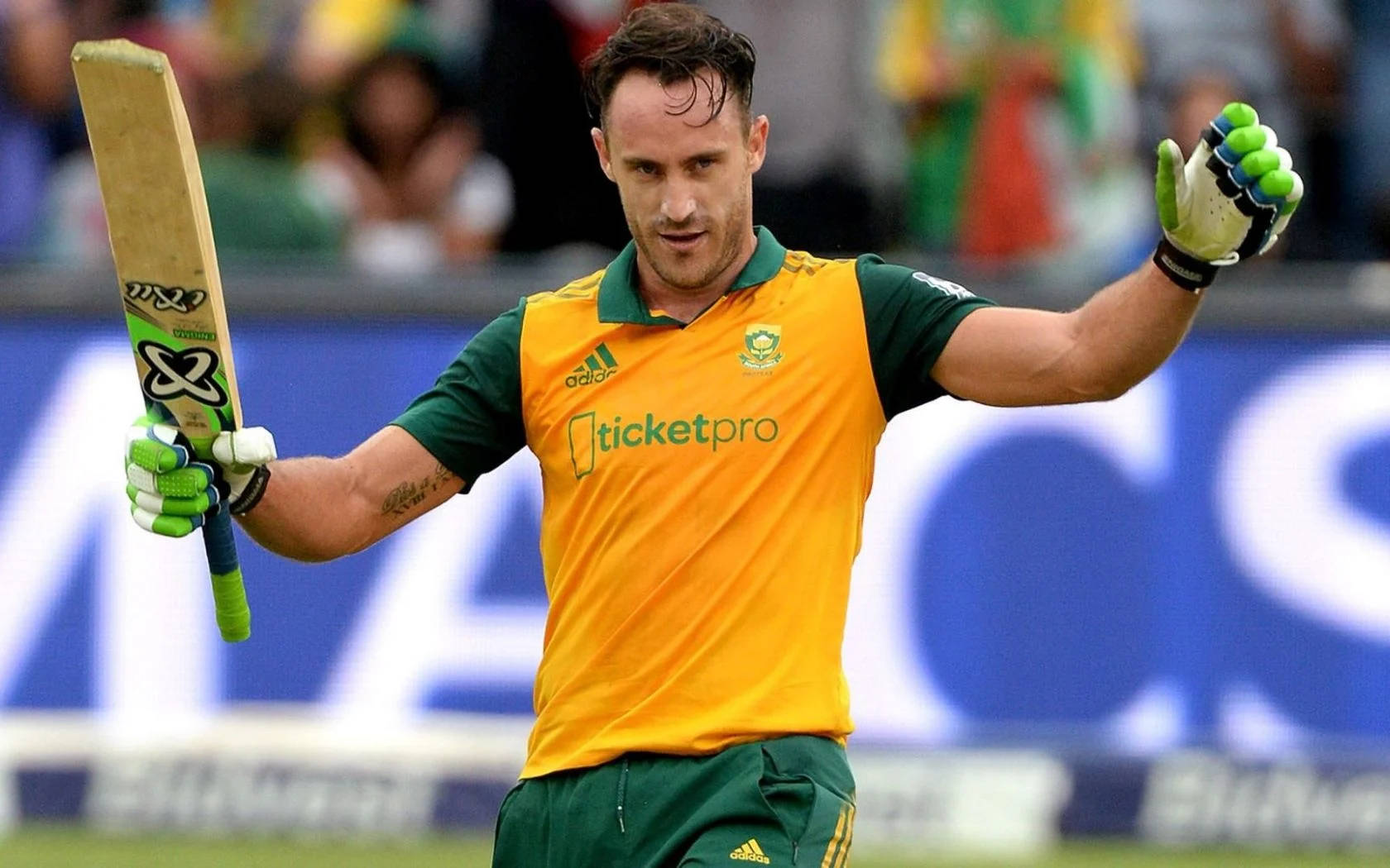 south africa cricket 桌布 壁紙 — 一名身穿黃綠色球衣的板球運動員在日間比賽中於球場上舉起球棒和戴手套的手。