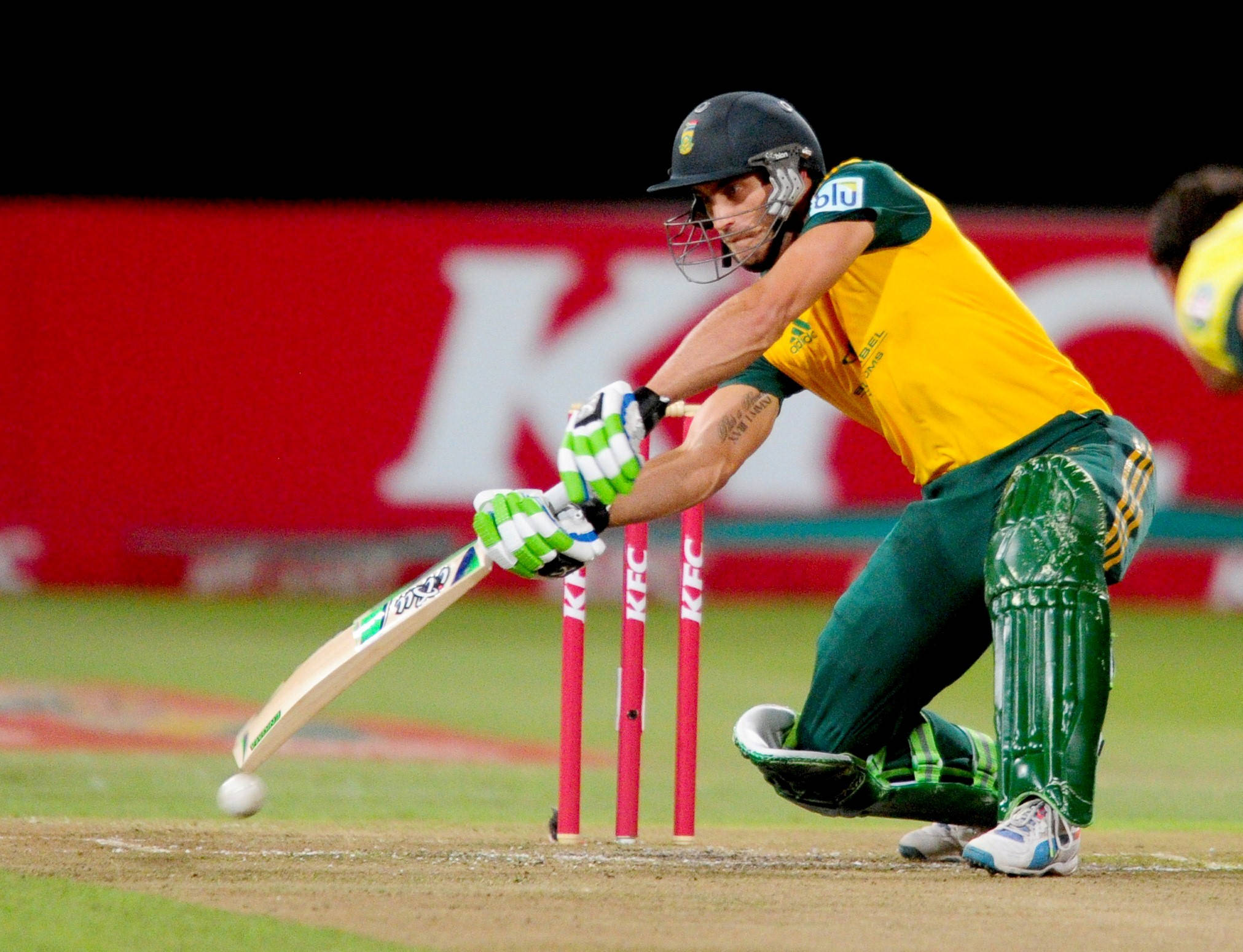 south africa cricket 桌布 壁紙 — 一名身穿黃綠色裝備的板球擊球手，在明亮的體育場燈光下，於夜間比賽中揮動球棒擊球。