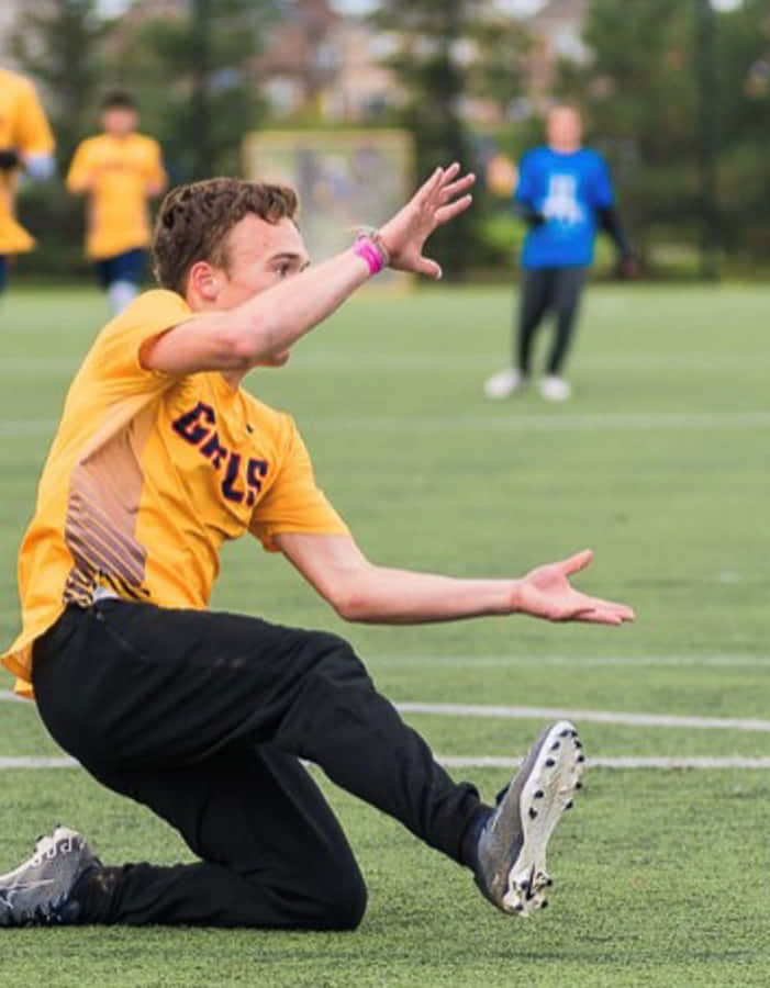 Android Ultimate Frisbee 桌布 壁紙 — 一名身穿黃色「GRS」球衣的年輕運動員在日間比賽中動態地飛撲過綠色運動場。