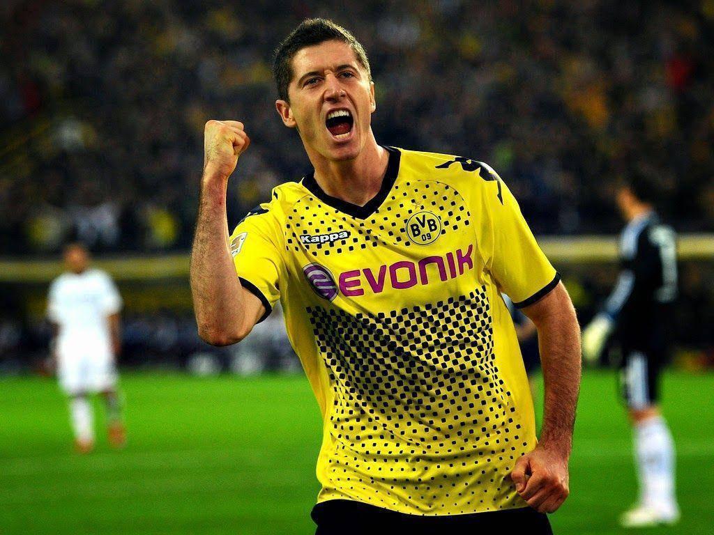 Lewandowski 桌布 壁紙 — 一名身穿黃色BVB球衣的足球運動員在球場燈光下的綠色草地上舉起拳頭張開嘴巴慶祝。