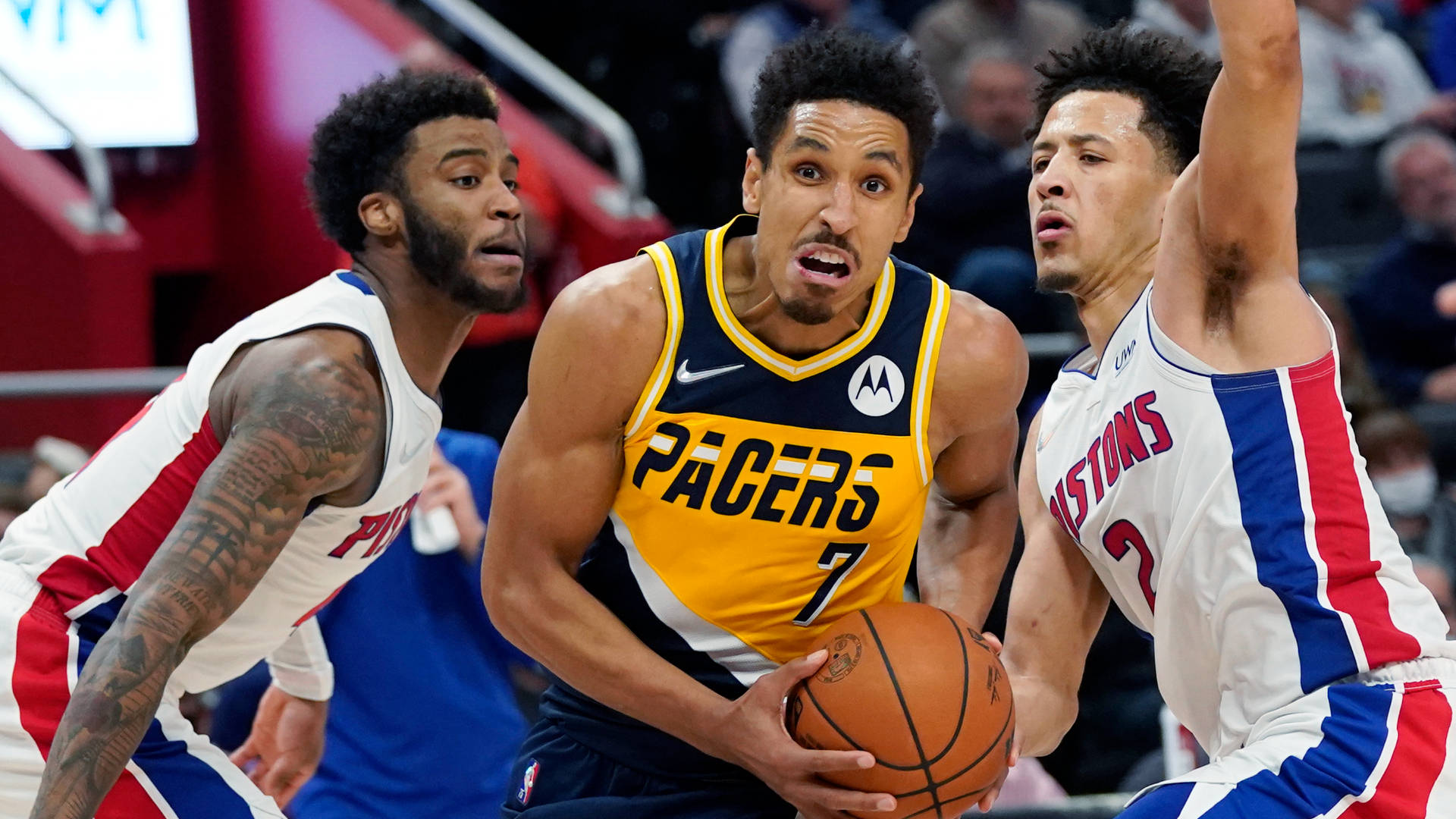 malcolm brogdon 桌布 壁紙 — 一名身穿黃色Pacers球衣的籃球運動員在擁擠的場館中運球，同時被兩名Pistons球員緊密防守。