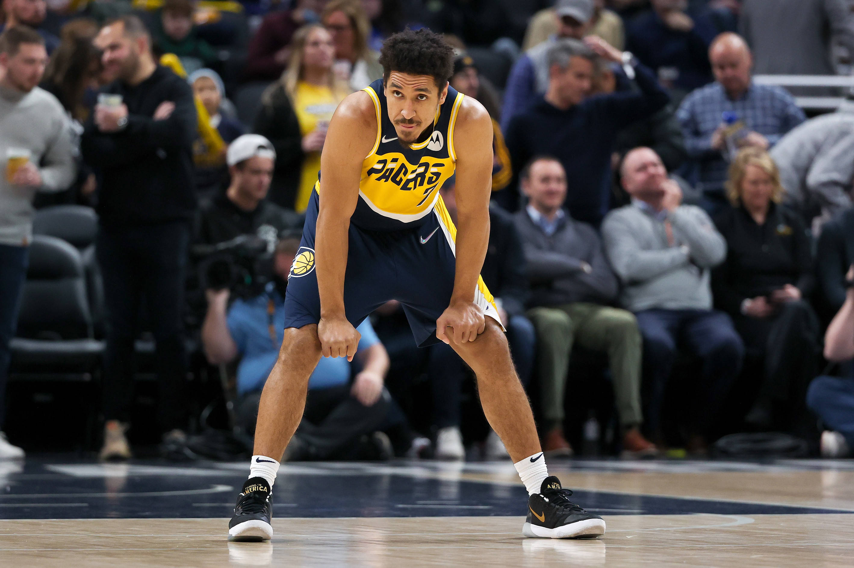 malcolm brogdon 桌布 壁紙 — 一名身穿黃色和海軍藍Pacers球衣的籃球運動員在拋光球場上低蹲，背景有模糊的觀眾。