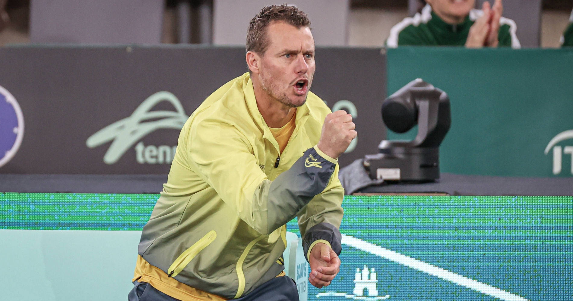 Australian Open 桌布 壁紙 — 一名身穿黃色外套的男網球運動員在燈光明亮的球場上握緊拳頭熱情慶祝。