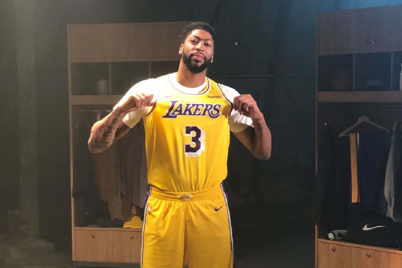 Anthony Davis 桌布 壁紙 — 一名身穿黃色湖人球衣、背號3的籃球運動員自信地站在燈光昏暗的更衣室裡。