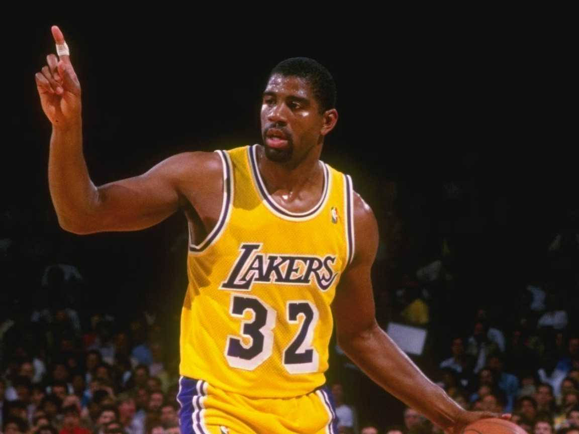 Magic Johnson 桌布 壁紙 — 一名身穿黃色湖人隊32號球衣的籃球運動員，在明亮的場館燈光下單手做手勢，同時拿著球。