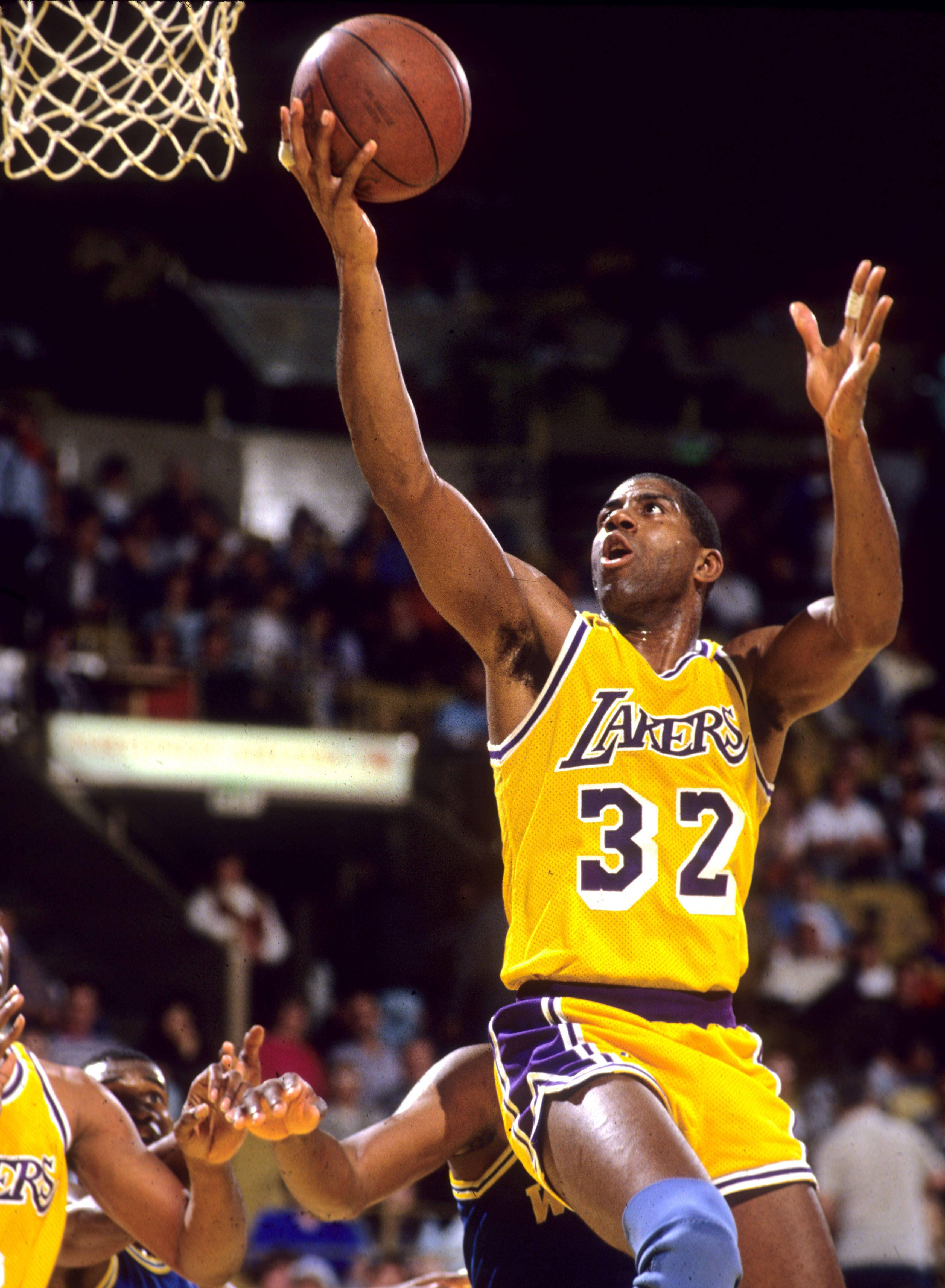 Magic Johnson 桌布 壁紙 — 一名身穿黃色湖人隊球衣、背號32的籃球運動員，手持籃球跳向籃框，防守球員在擁擠的場館中伸手阻擋。