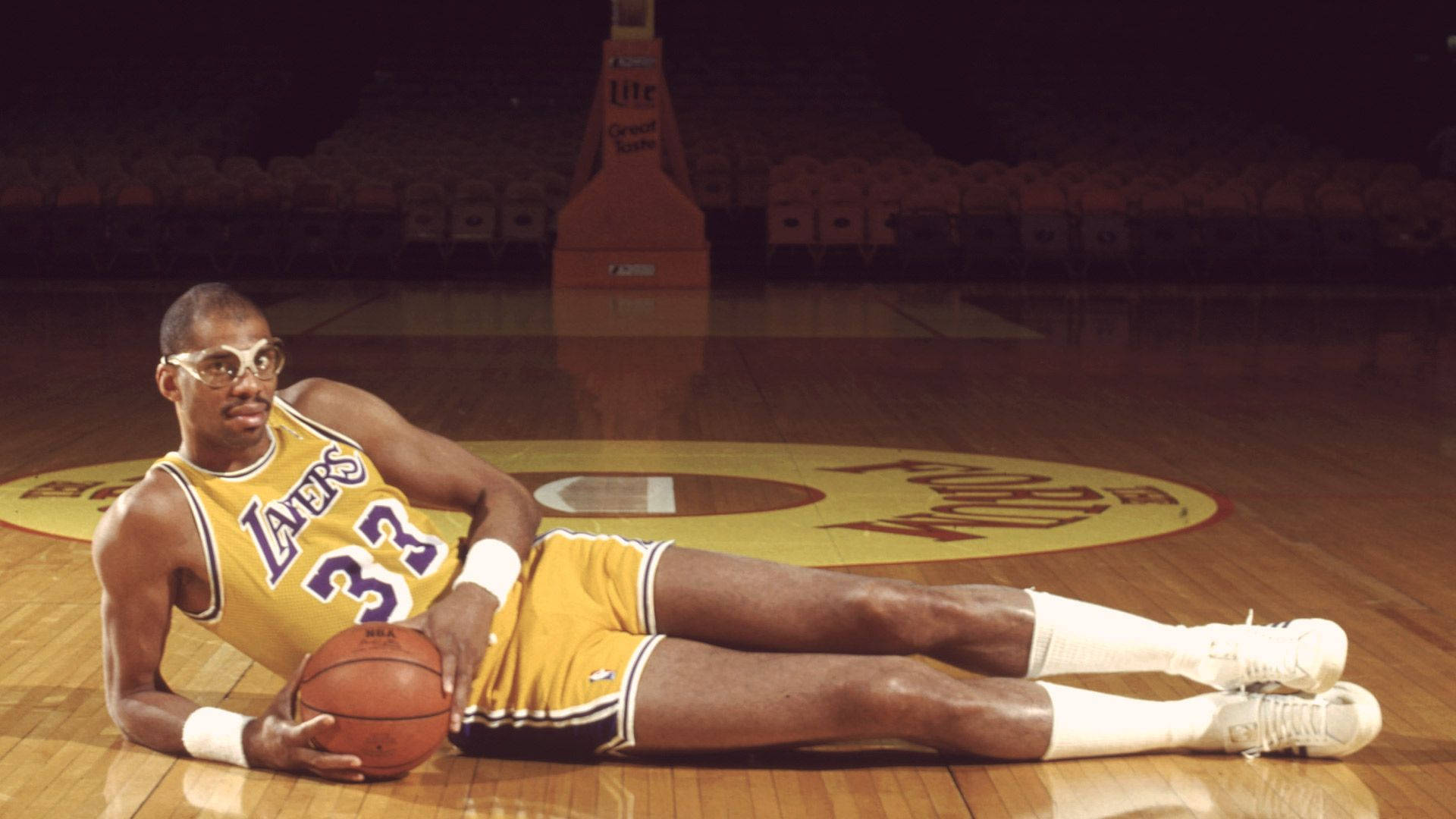 Kareem 桌布 壁紙 — 一名身穿黃色湖人隊球衣的籃球運動員躺在拋光木地板上，專注地拿著球。