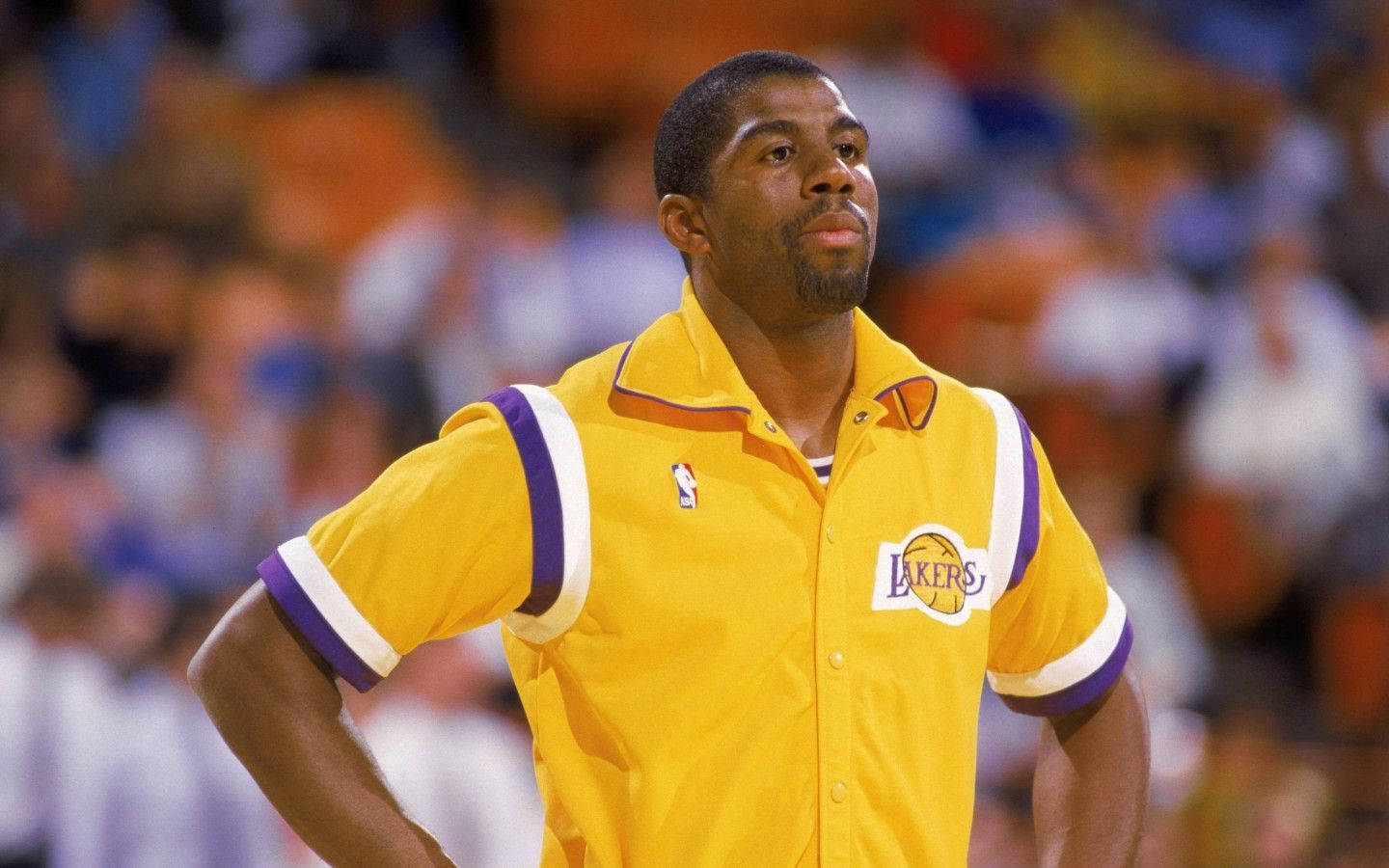 Magic Johnson 桌布 壁紙 — 一名身穿黃色湖人隊球衣的籃球運動員在比賽中雙手叉腰站立，背景是模糊的人群。