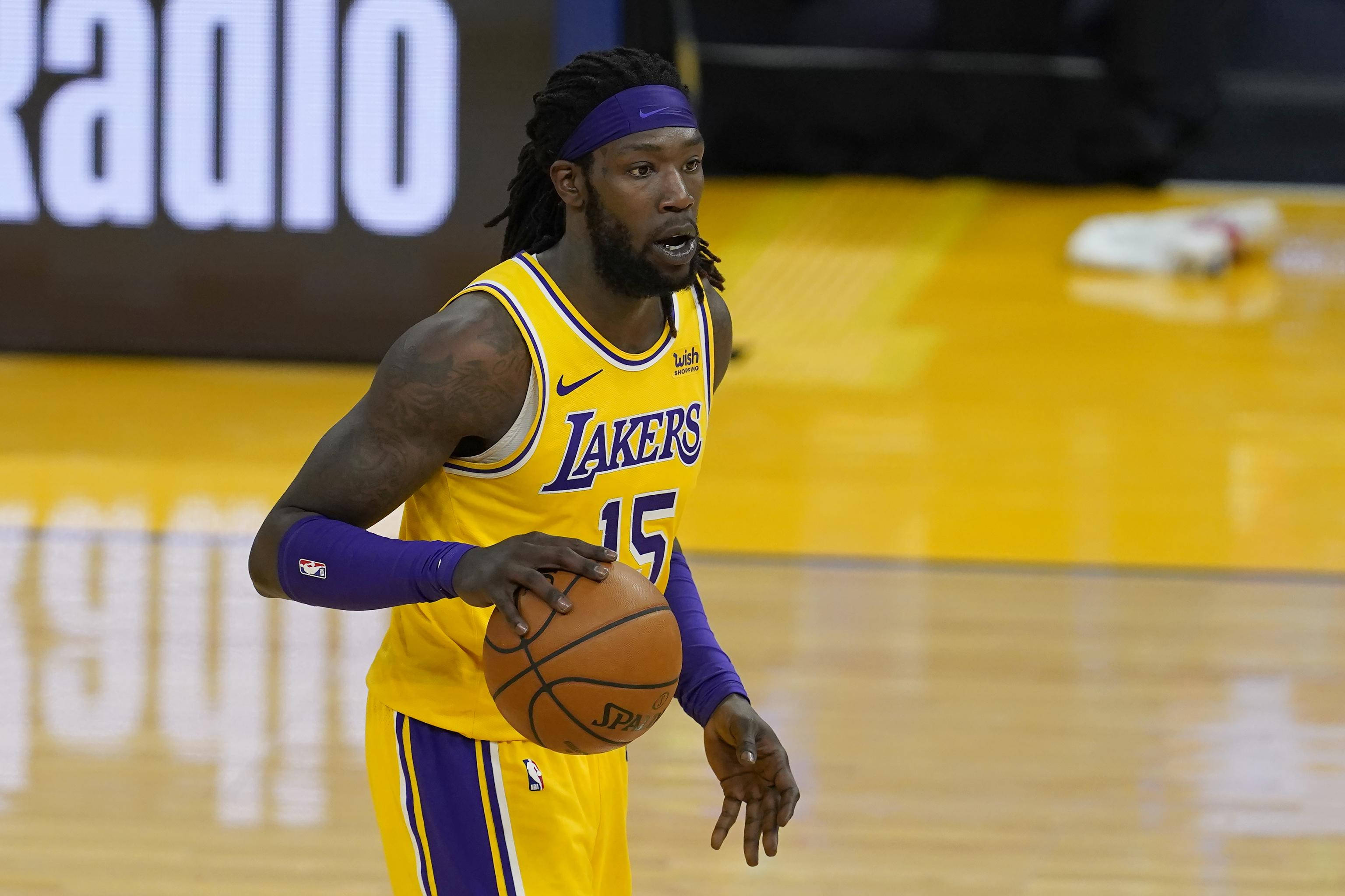 montrezl harrell 桌布 壁紙 — 一名身穿黃色湖人隊球衣的籃球運動員在明亮的場館燈光下，於拋光球場上運球。