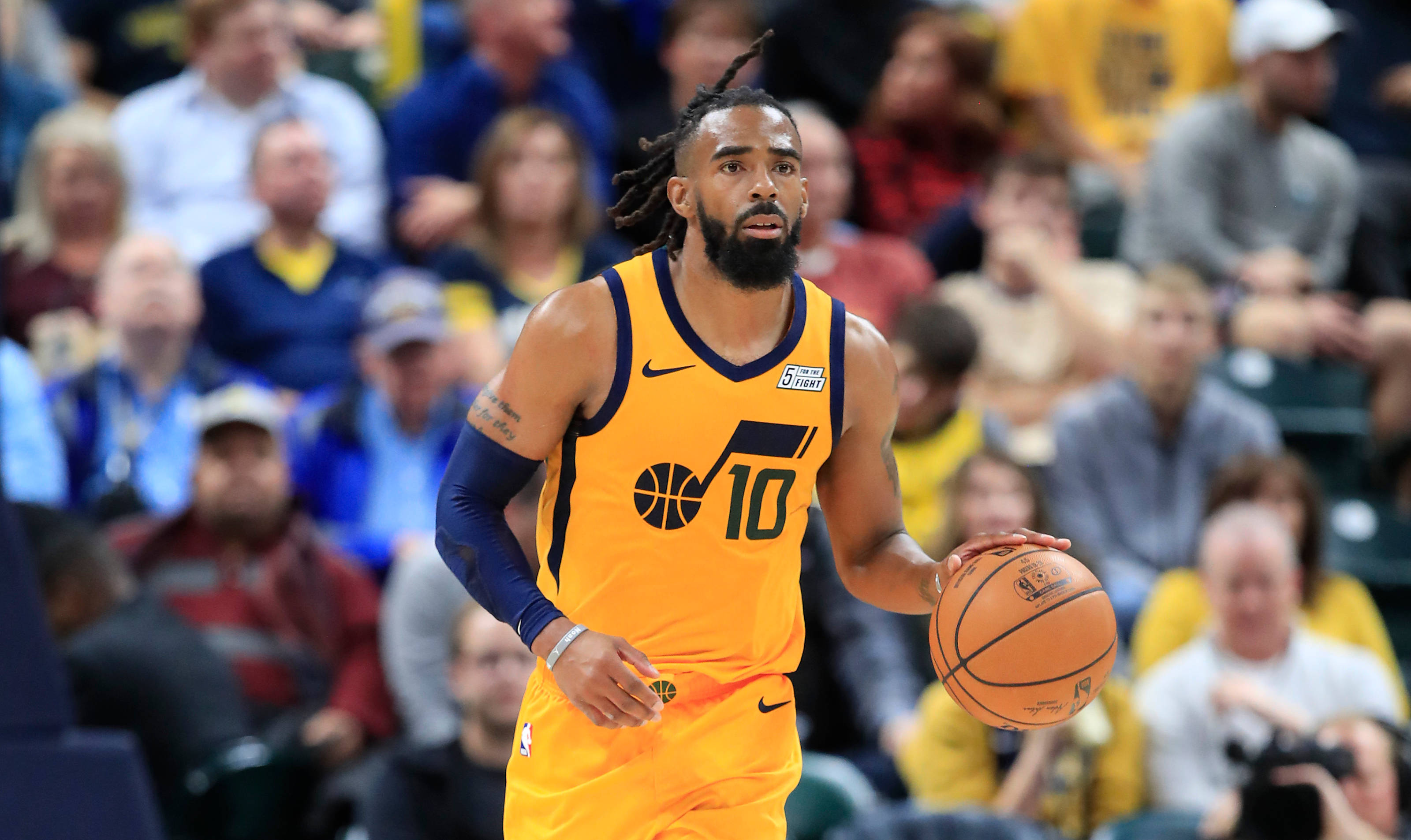 mike conley 桌布 壁紙 — 一名身穿黃色球衣、專注的籃球運動員在激烈的比賽中運球，背景是模糊的人群。
