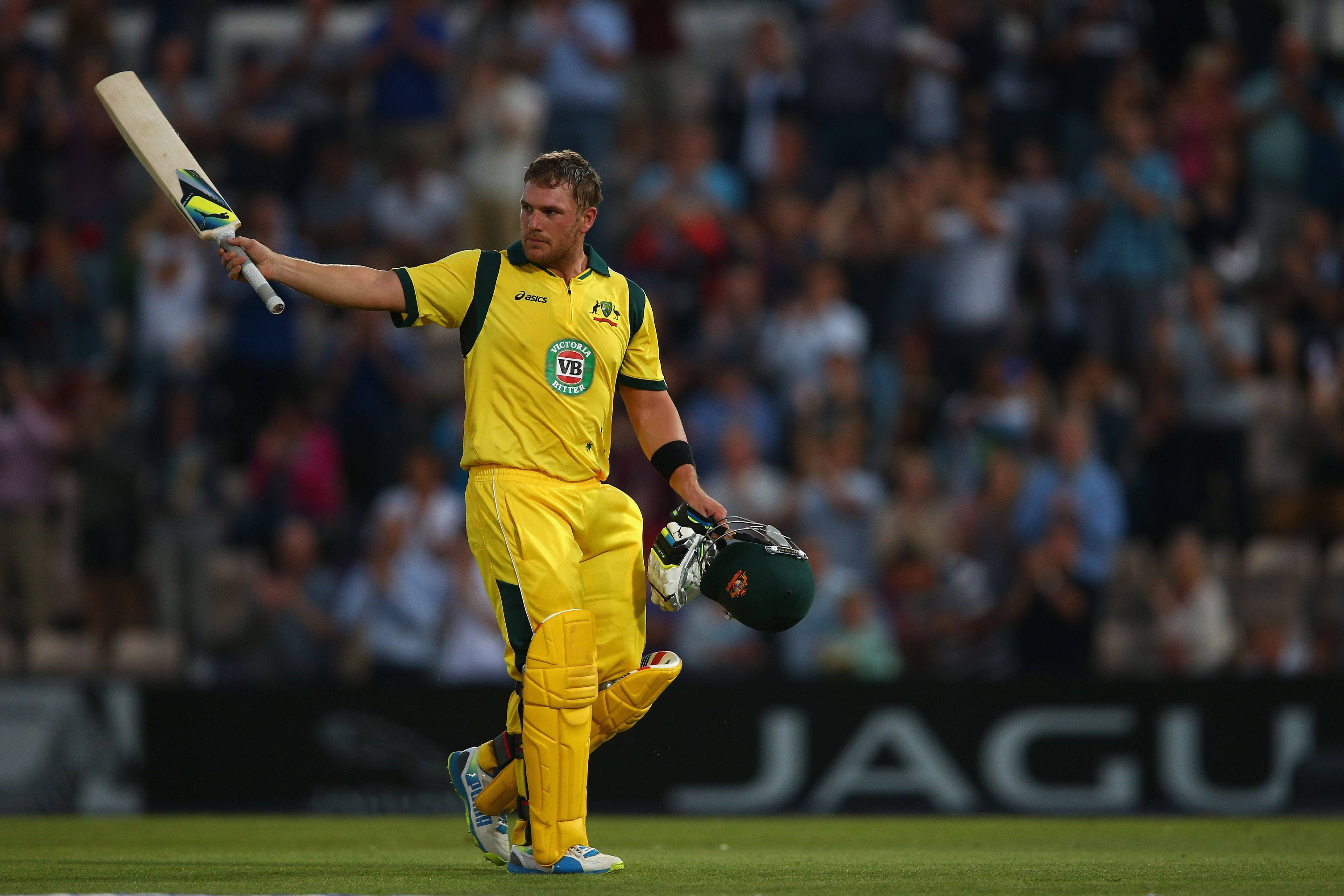 Aaron Finch 桌布 壁紙 — 一名身穿黃色球衣的澳洲板球運動員在球場燈光下手持球棒和頭盔離場。