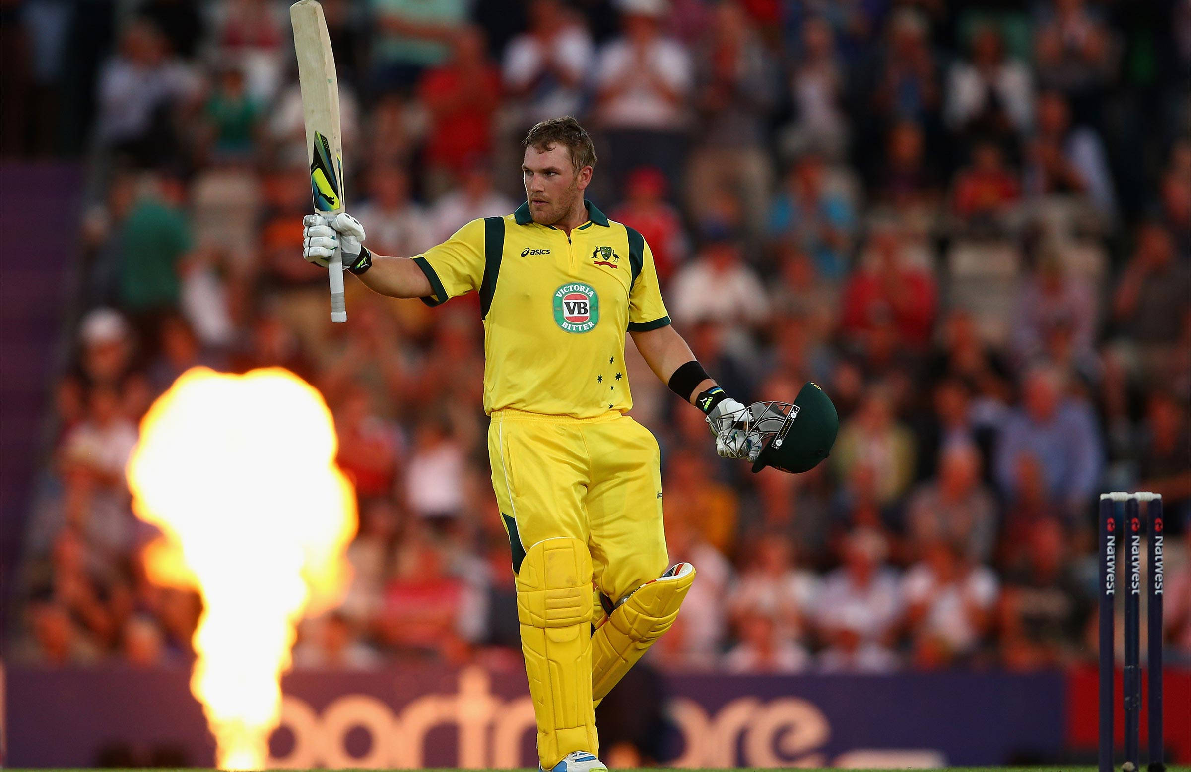 Aaron Finch 桌布 壁紙 — 一名身穿黃色球衣的澳洲板球運動員在球場燈光下取得百分後，手持球棒和頭盔慶祝。