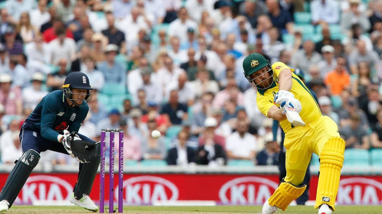 Aaron Finch 桌布 壁紙 — 一名身穿黃色球衣的澳洲板球選手揮動球棒擊球，而一名英格蘭守門員在明亮的日光下蹲在球門後方。