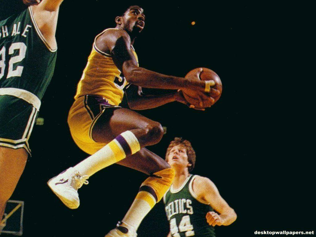 Magic Johnson 桌布 壁紙 — 一名身穿黃色球衣的籃球運動員在空中躍起抓住球，而身穿綠色球衣的防守球員試圖在黑色背景下阻擋他。