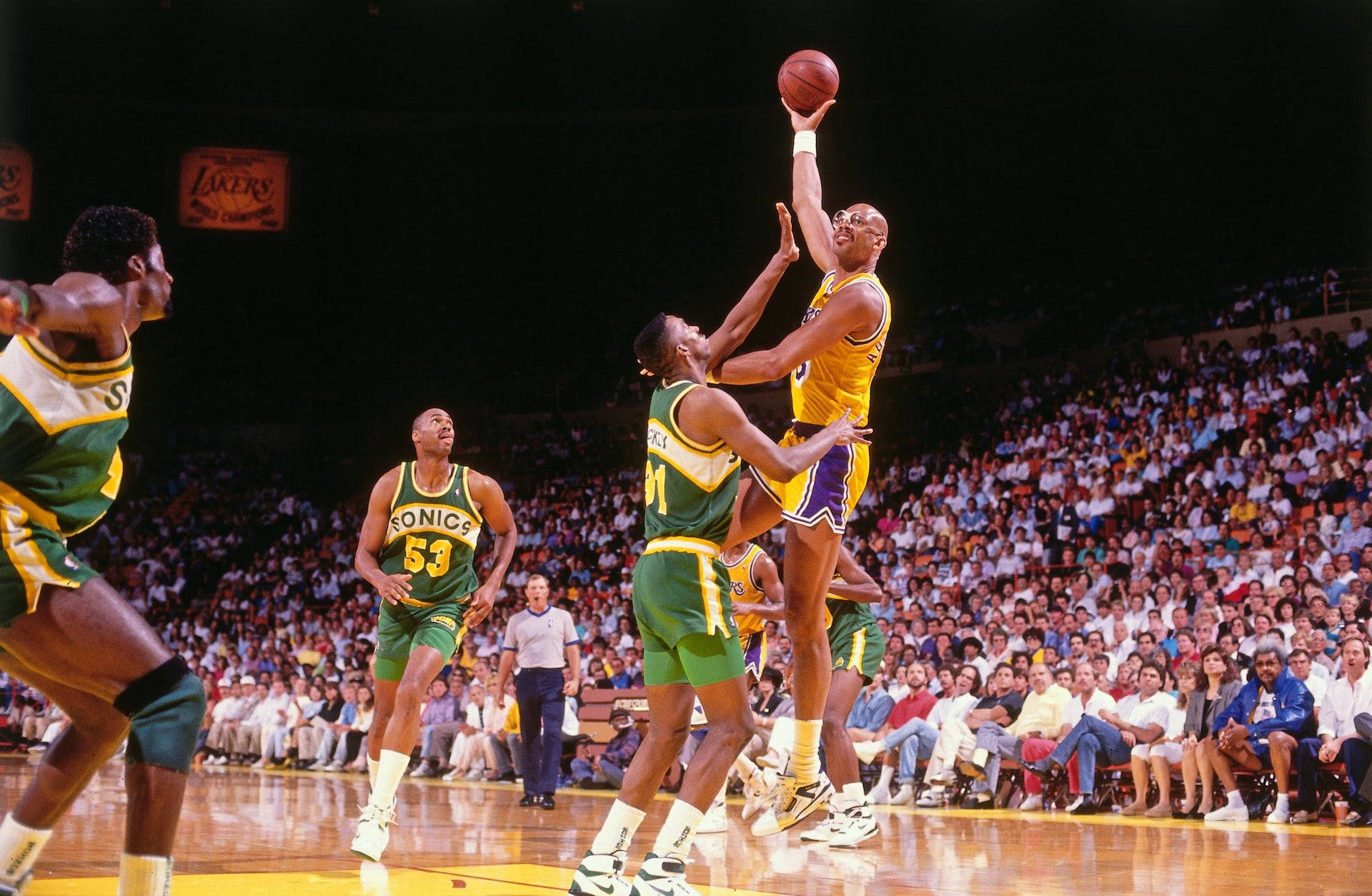 Kareem 桌布 壁紙 — 一名身穿黃色球衣的籃球運動員跳起投籃，而身穿綠色球衣的防守球員在擠滿觀眾的場館比賽中試圖封阻他。